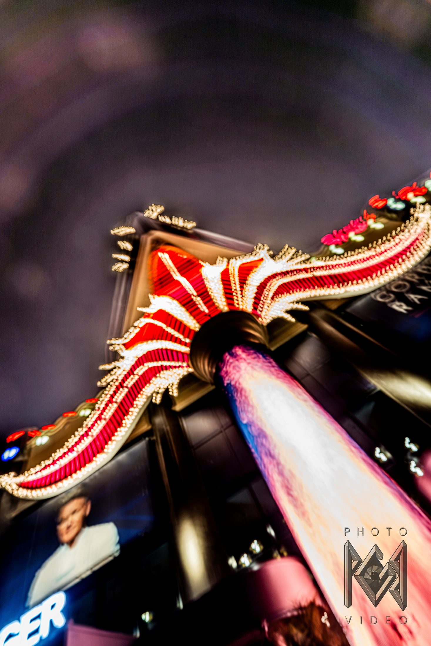 Looking up at a red and gold lit sign and a pink-lit pillar, slightly blurred against the night sky