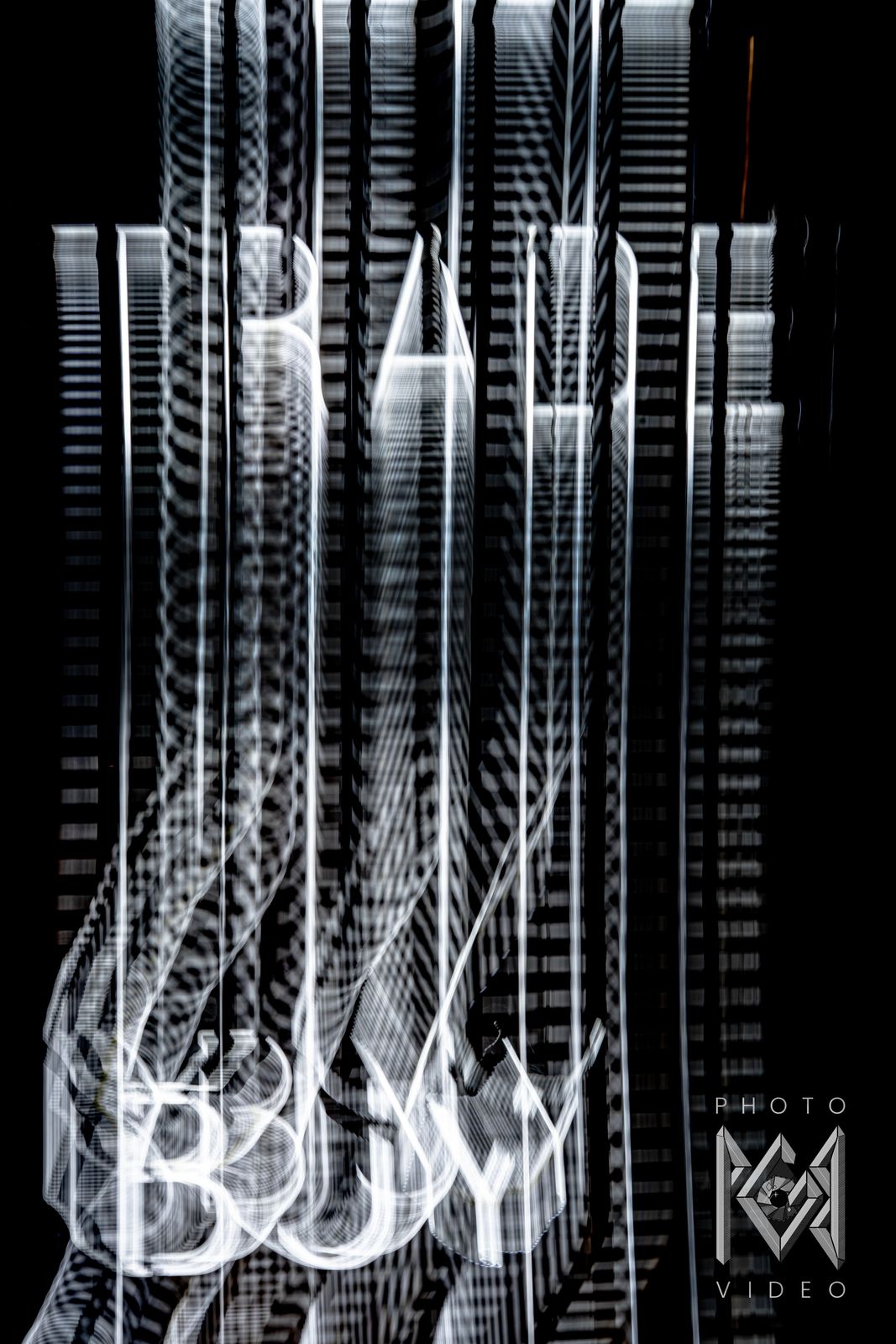 White sign lettering stretched into tall streaks by a moving camera, with BUY glowing near the bottom