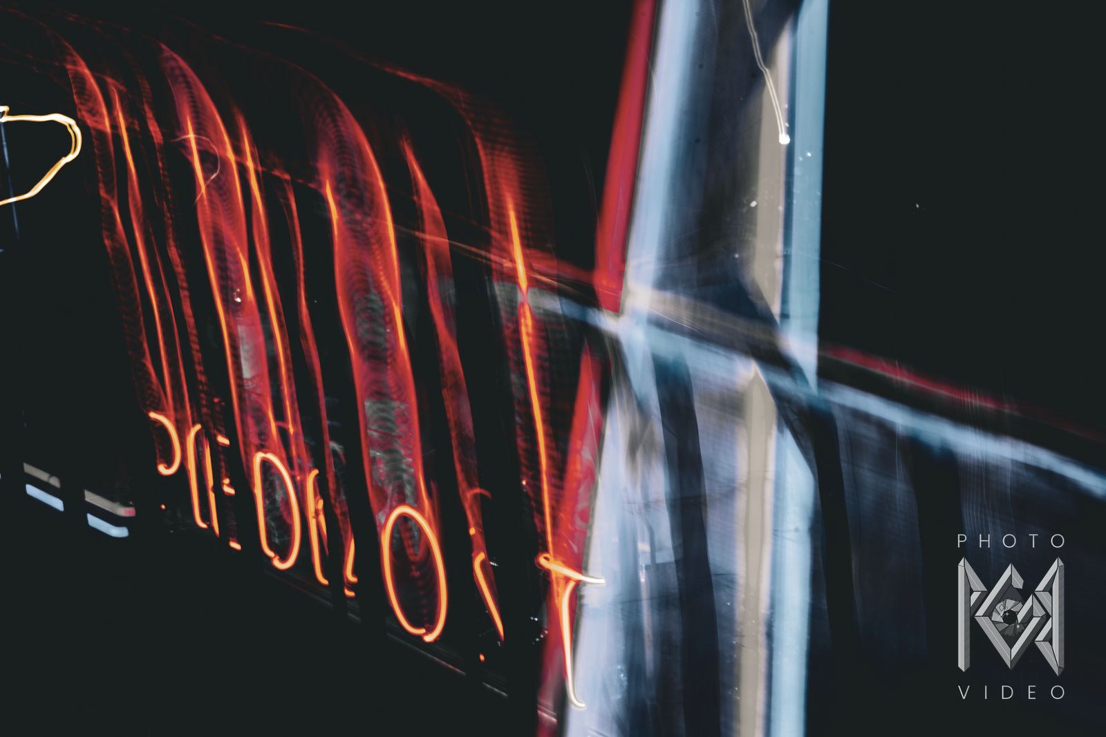 Orange neon lettering drawn into tall streaks beside a pale blur of light
