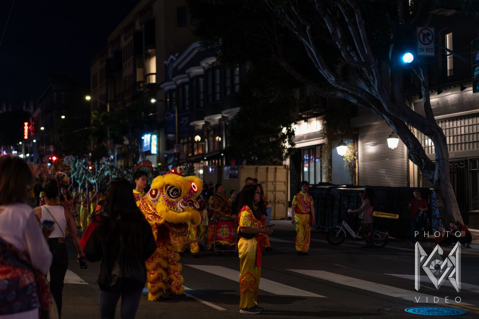A yellow lion dancer and performers in red and gold costumes crossing the street at night
