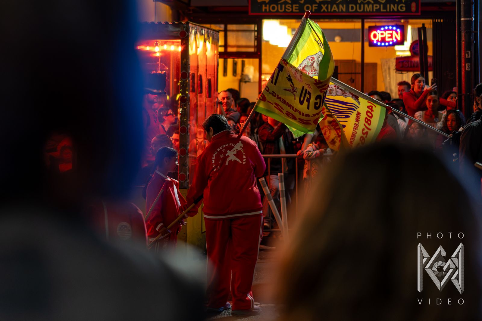 A kung fu performer in a red tracksuit swinging a yellow school flag in front of a crowd