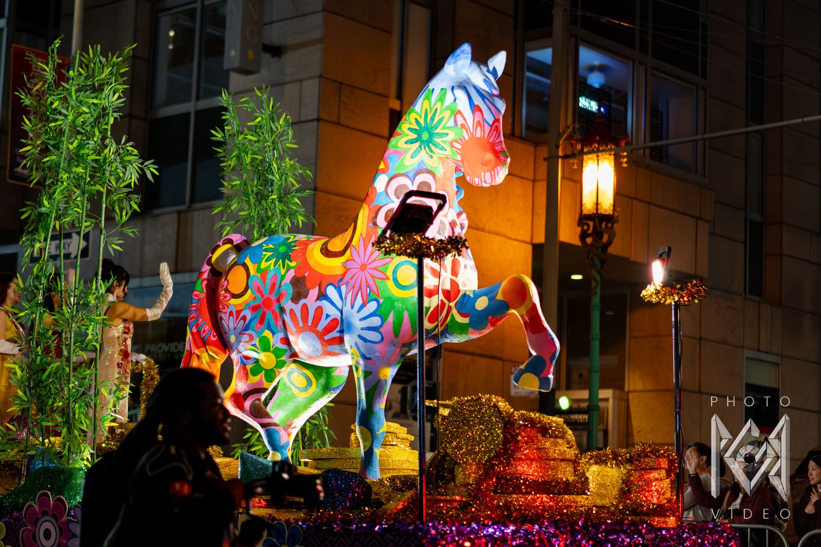 A tall horse statue painted with bright flowers on a float lined with bamboo and gold tinsel