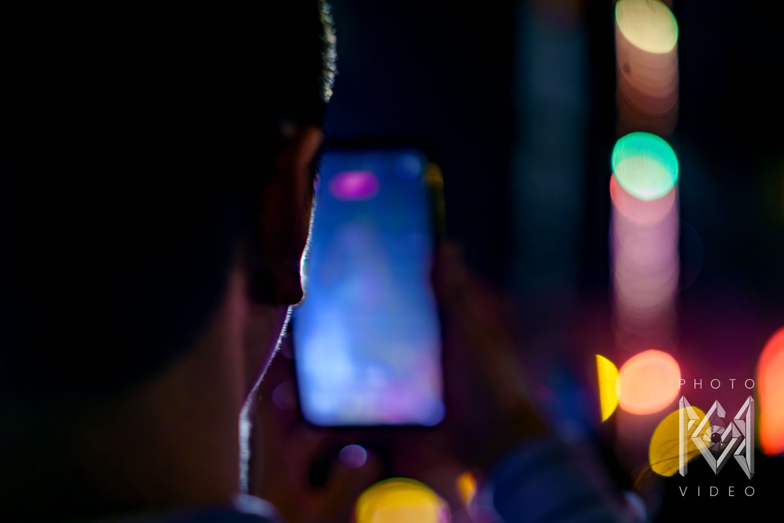 A spectator in silhouette filming the parade on a phone against blurred coloured lights