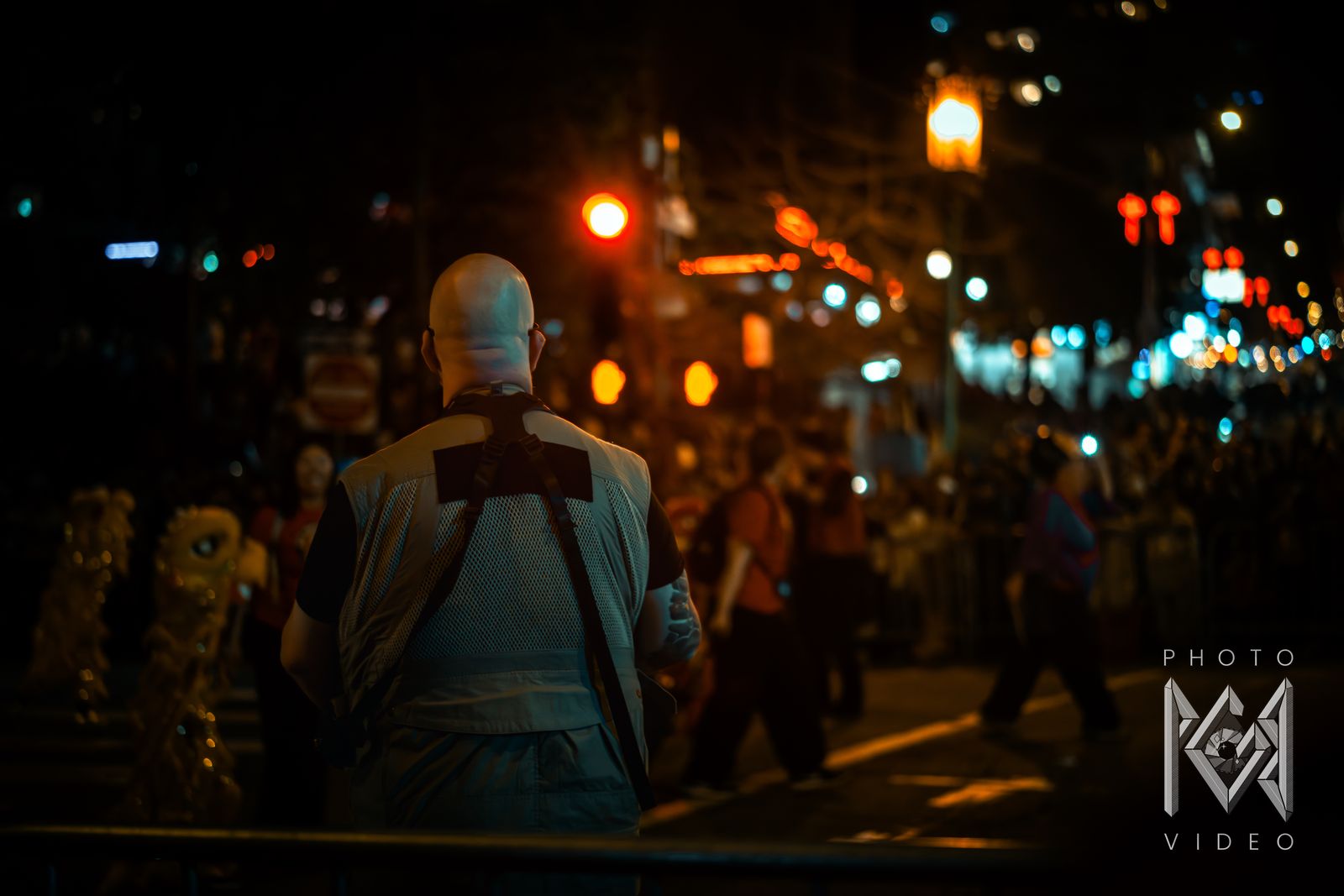A spectator in a costume cape watching the parade pass down a lantern-lit street