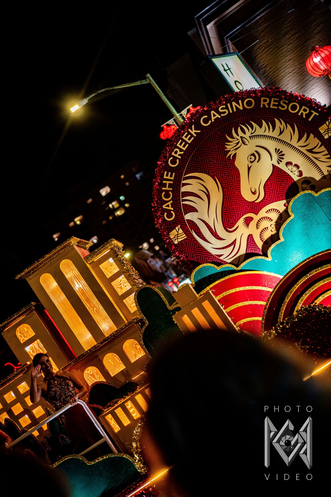 A tilted view of a float with a golden horse emblem and glowing model buildings, lit by a street lamp