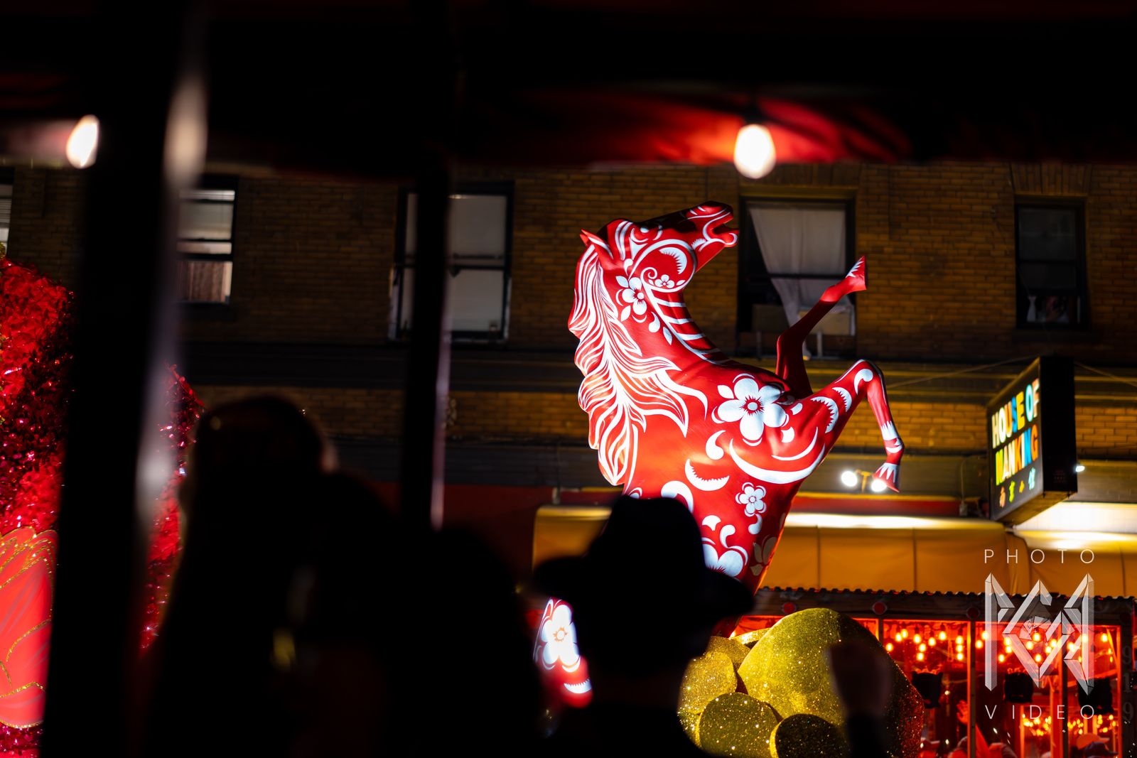 A red horse float painted with white flowers rearing above the crowd outside the House of Nanking