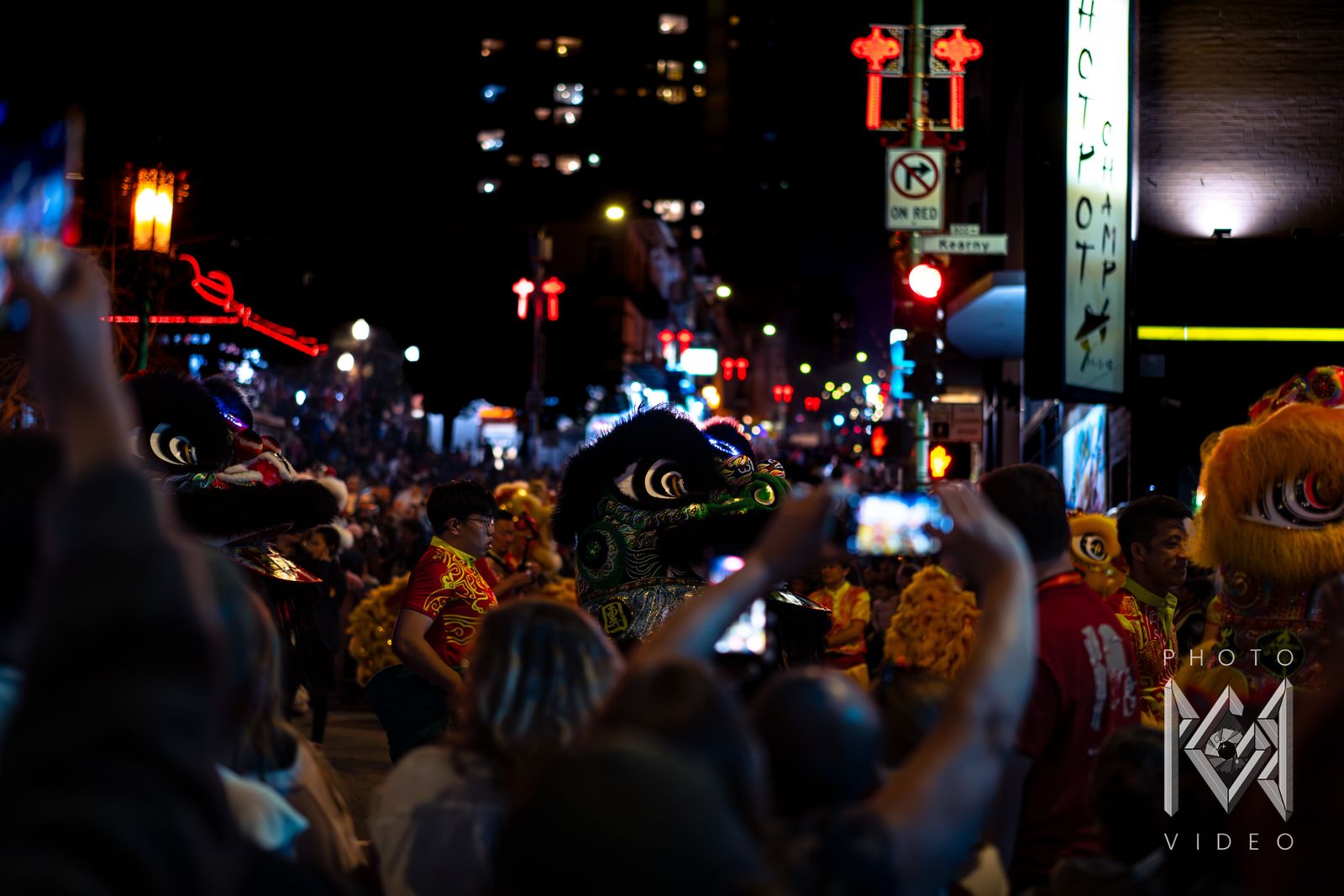 Black, green and yellow lion dancers crowding Kearny Street under red lantern lights as spectators film