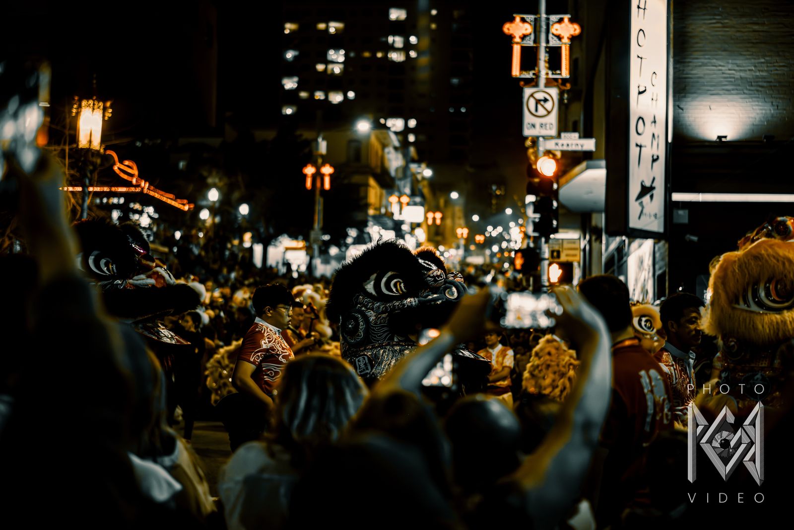 Black and yellow lion dancers crowding Kearny Street as spectators film, in muted amber tones