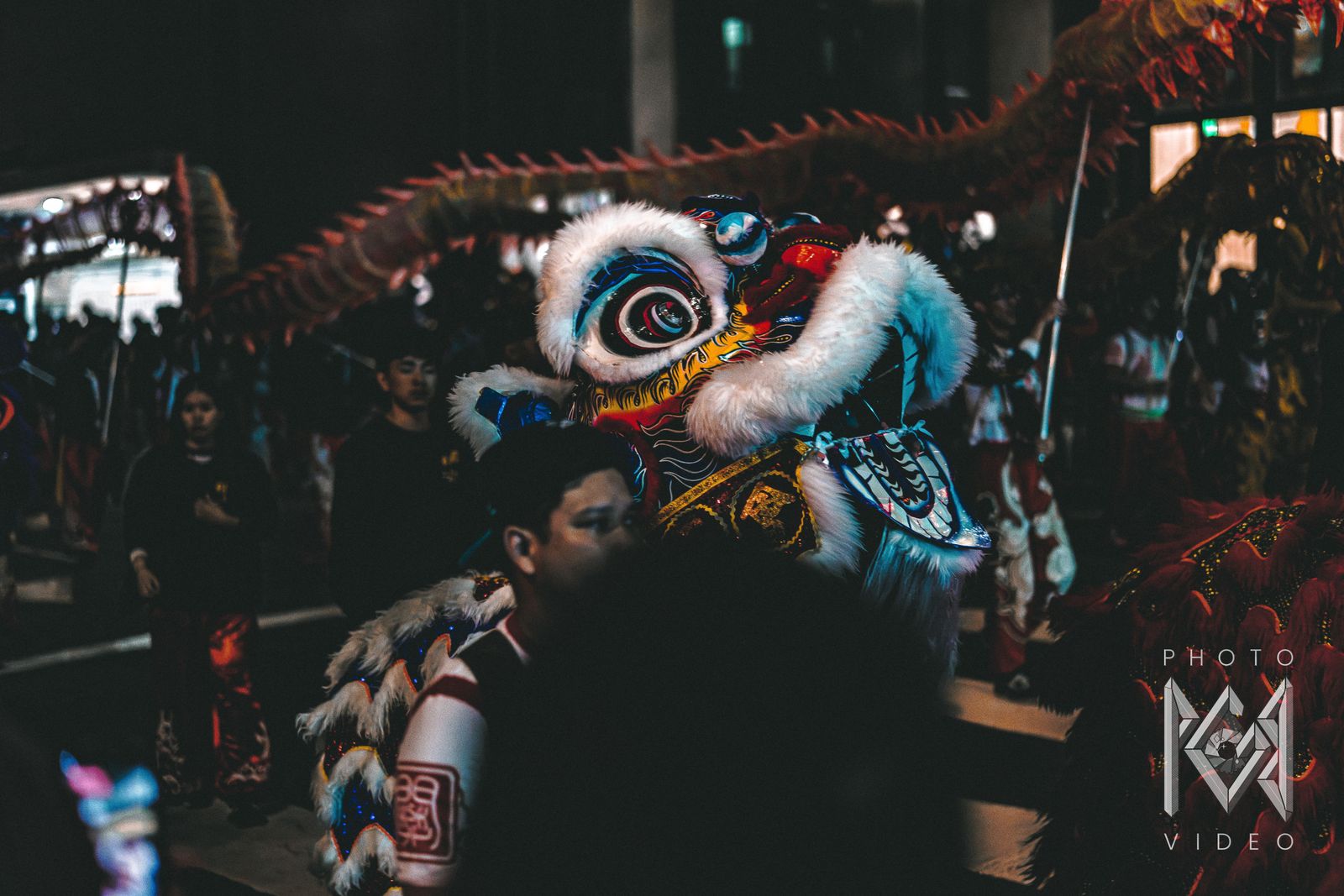 A blue-eyed lion dance head beside a dancer, with a long red dragon passing overhead