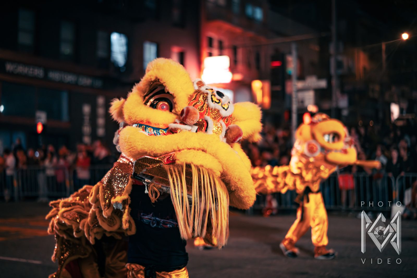 A yellow lion dance head in close-up, with a second yellow lion dancing behind it