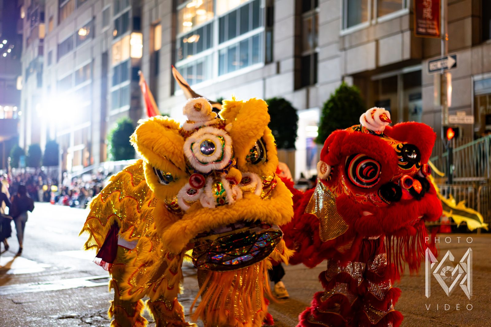 A yellow lion and a red lion facing the camera on a brightly lit street