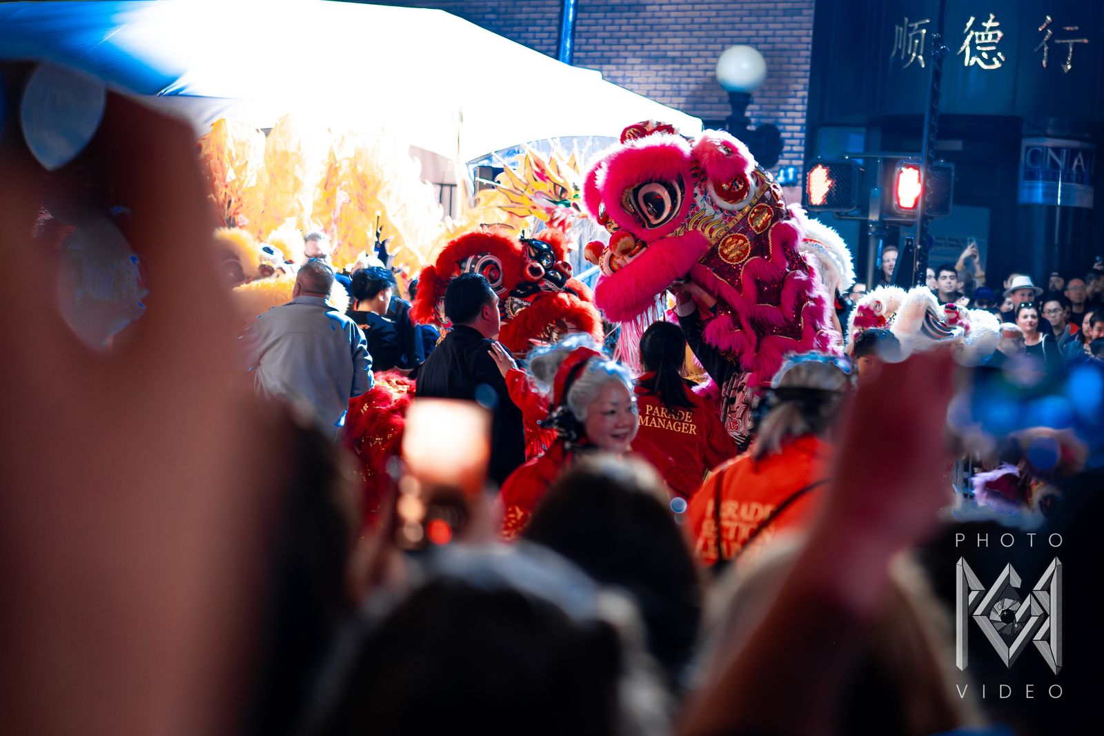 A pink lion dance head among parade managers and dancers in front of a bright tent