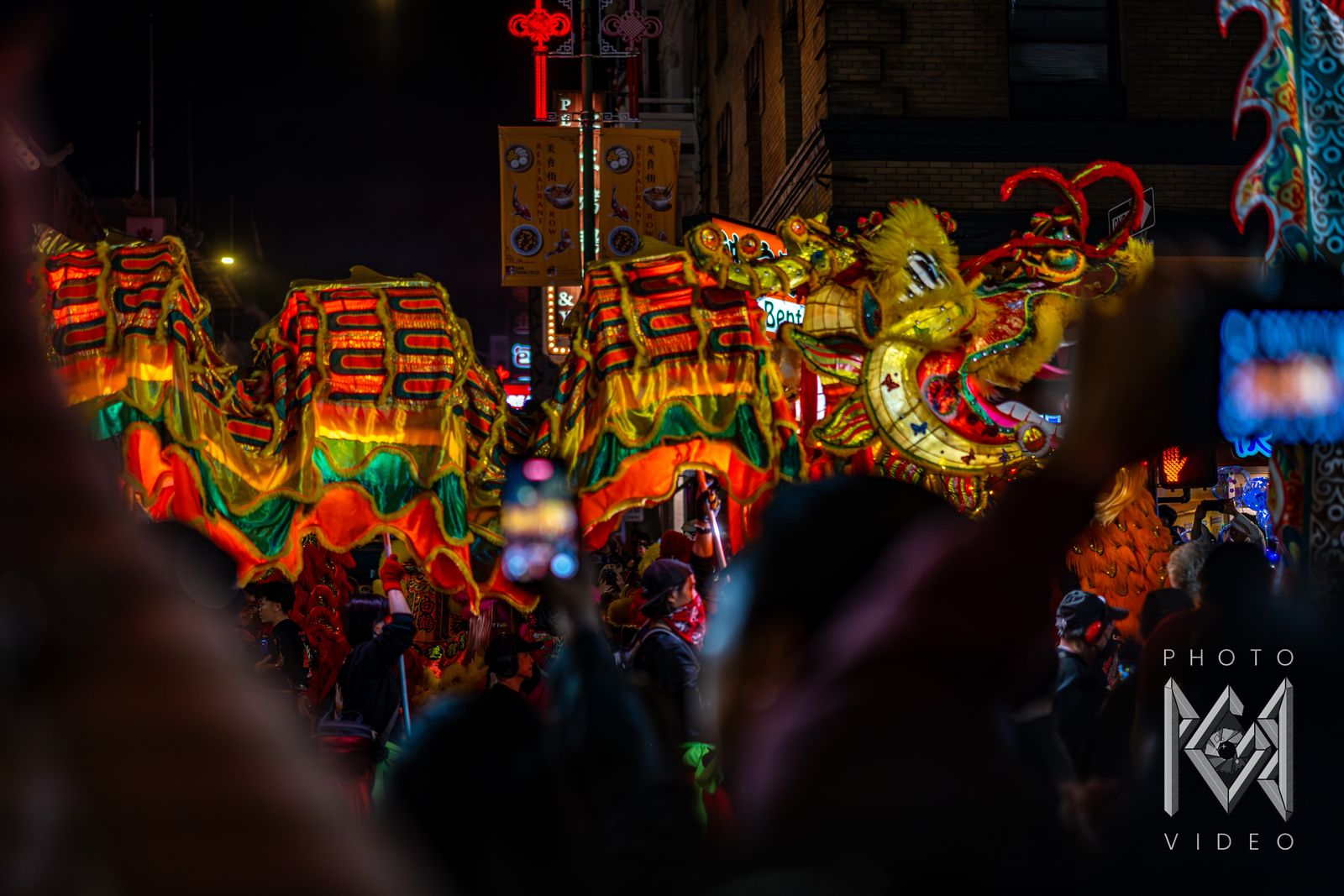 A glowing dragon winding through the crowd under Chinatown signs, its head rearing to the right