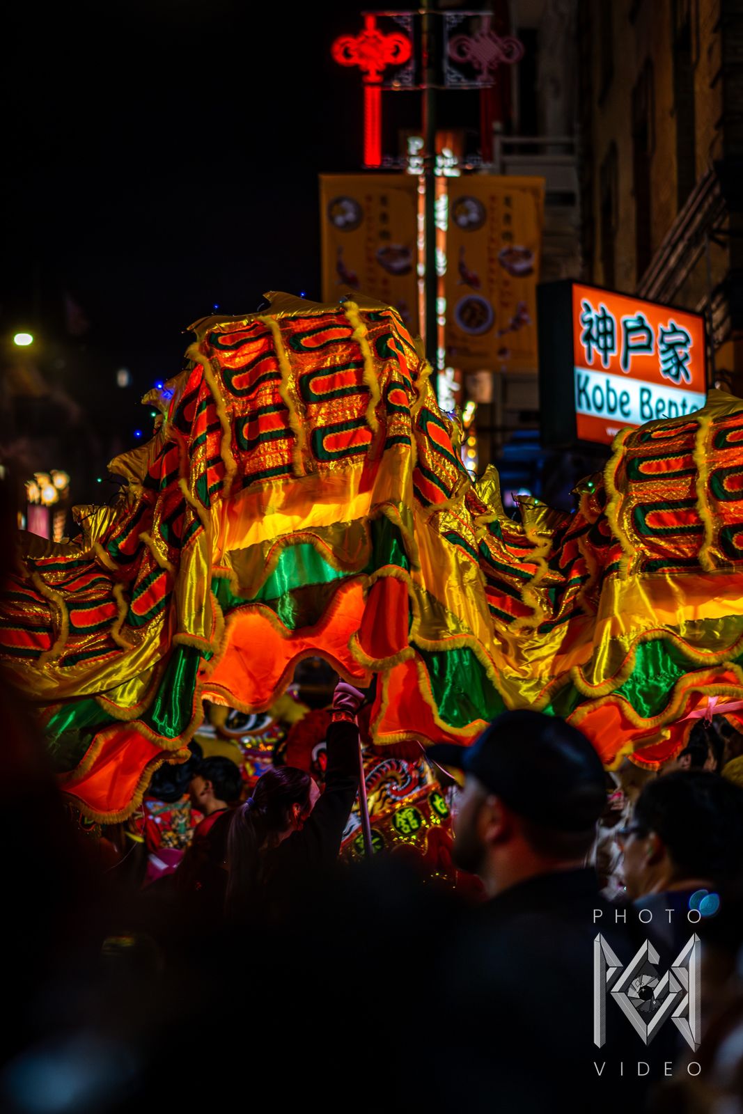 The glowing striped body of a dragon arching above the crowd beside the Kobe Bento sign