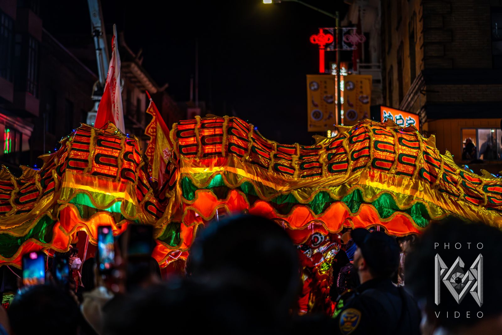 The glowing body of a dragon rippling above a crowd holding up phones, under red lantern lights