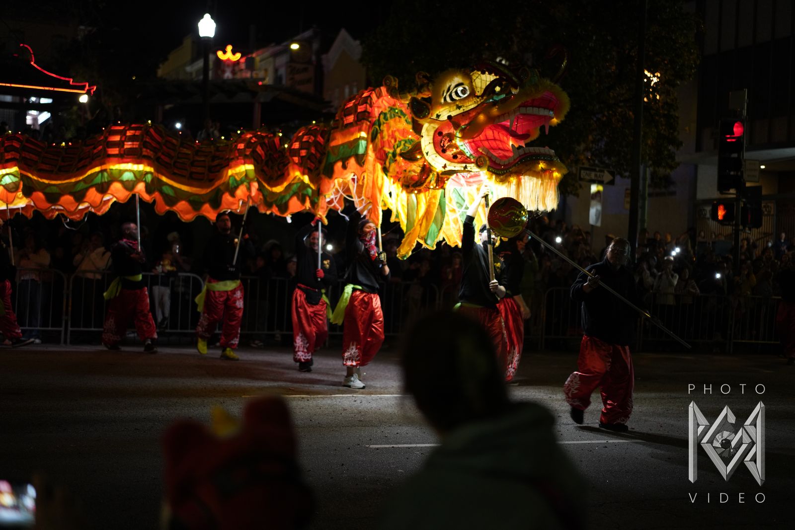 Dancers in red trousers carrying a glowing dragon down a dark street, led by a dancer with the pearl, as the crowd looks on