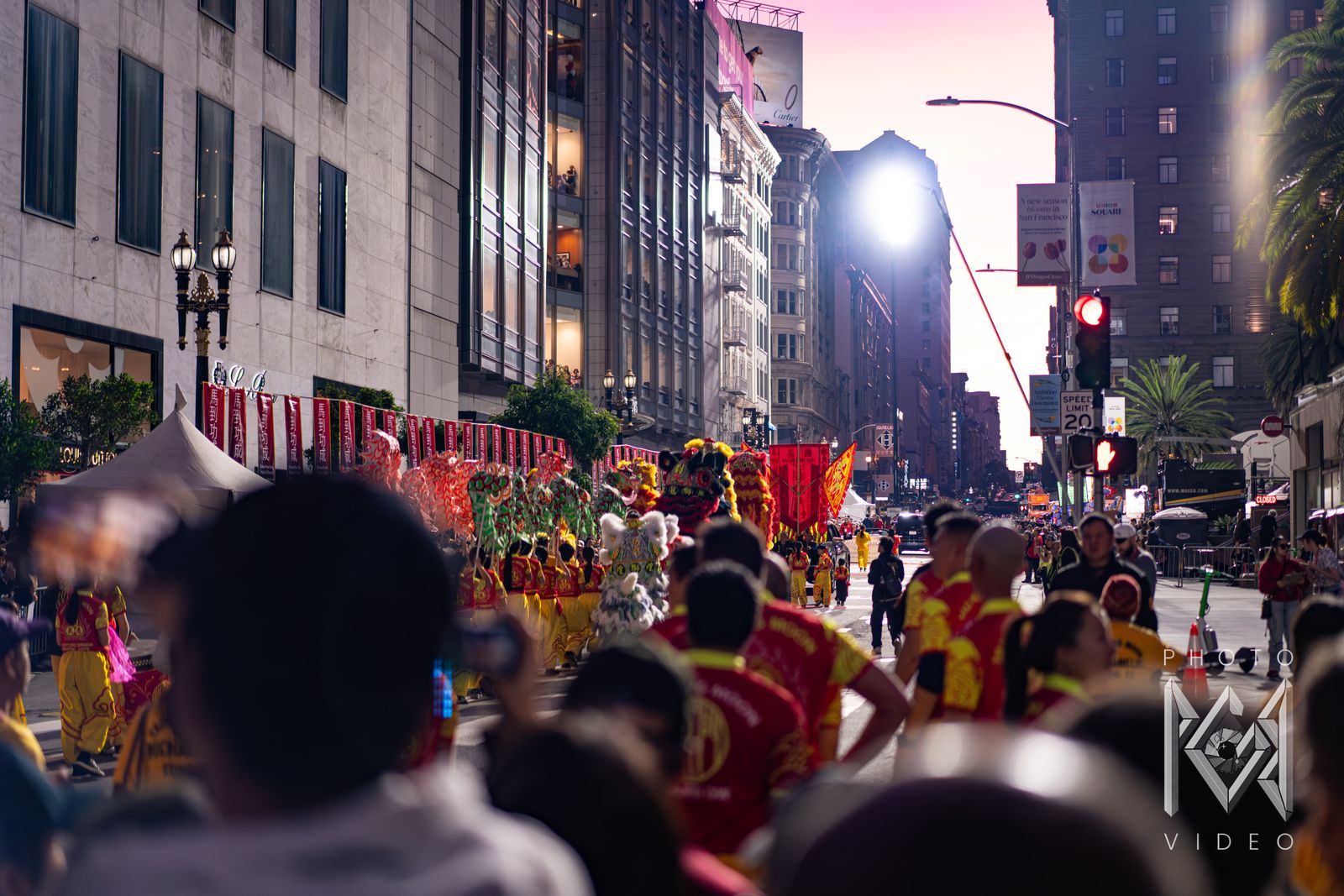 Lion dancers and performers in red and yellow filling Union Square's street at sunset, with red banners along the shops