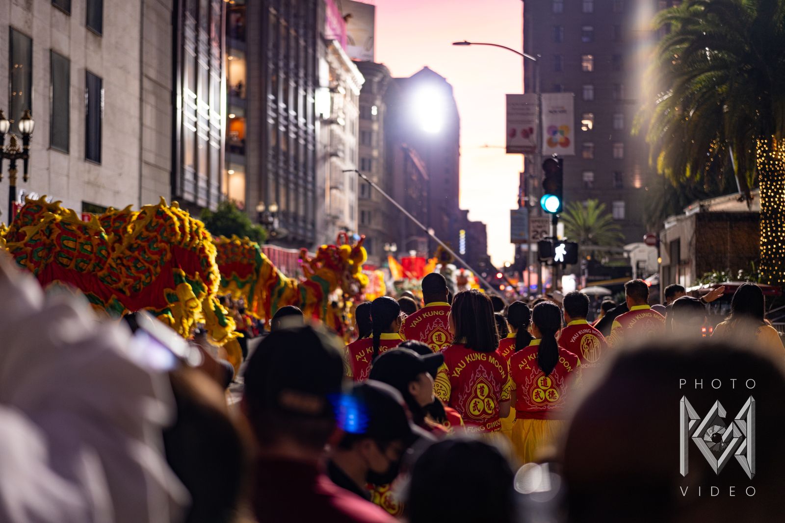 Performers in Yau Kung Moon jerseys following a red and gold dragon down the street at sunset