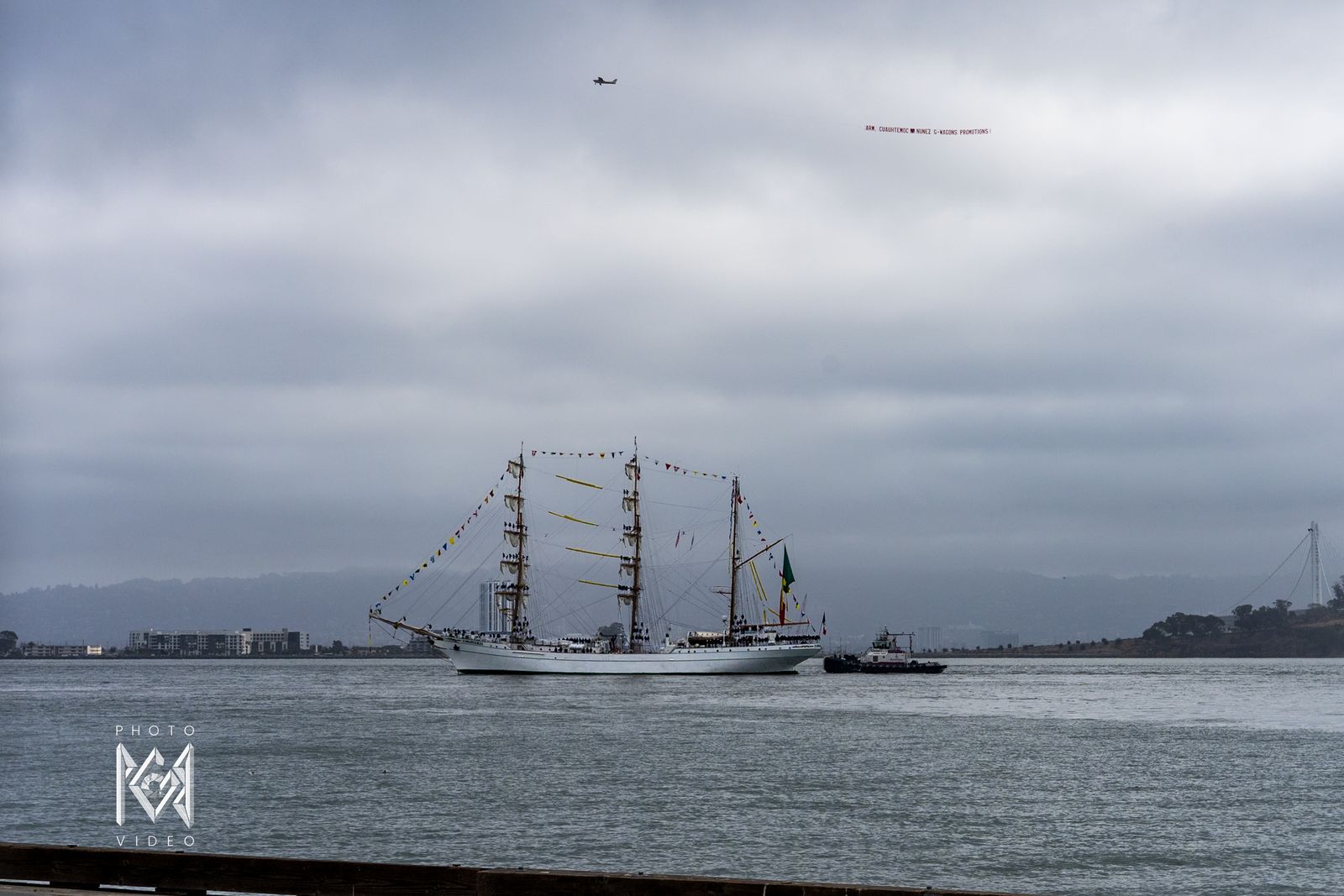 The ship in the bay with a tug alongside, an airplane towing a banner overhead
