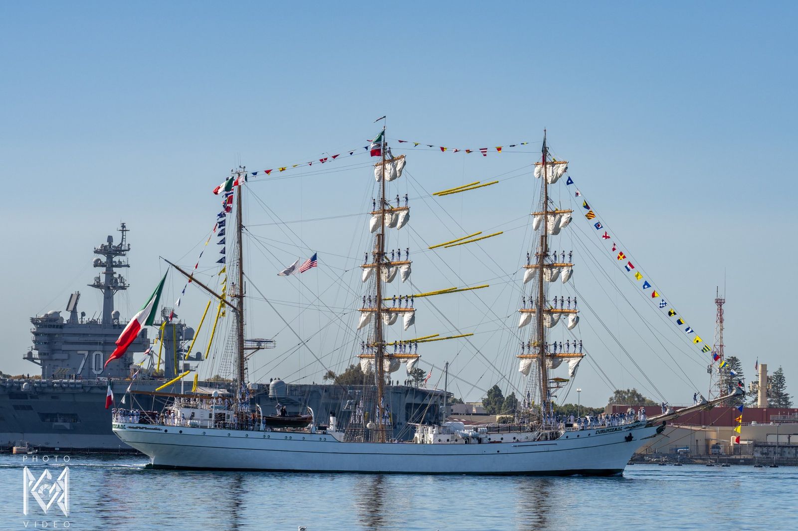 The tall ship dressed in flags passing an aircraft carrier at the naval base