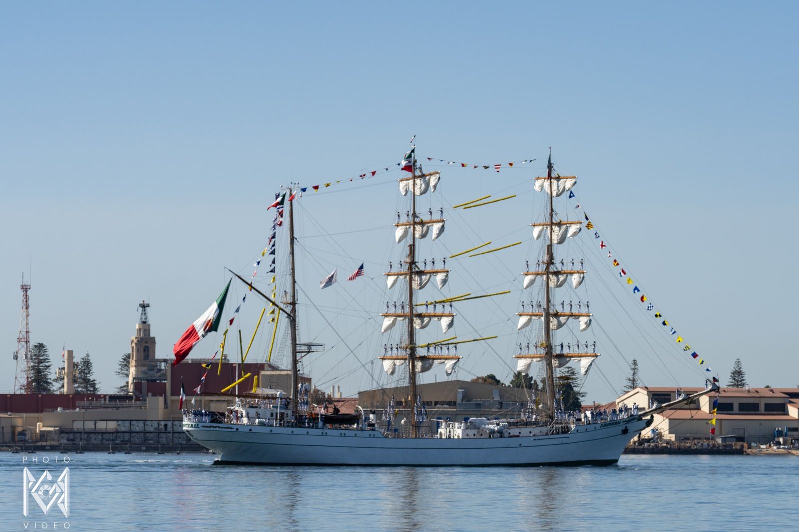 The tall ship passing the harbour shore with signal flags strung from her masts