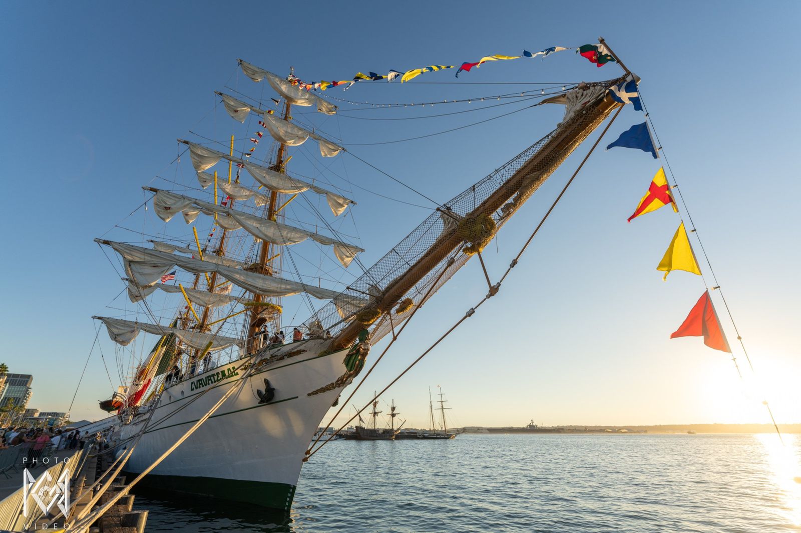 The bow and bowsprit with signal flags in low sun beside the sparkling bay