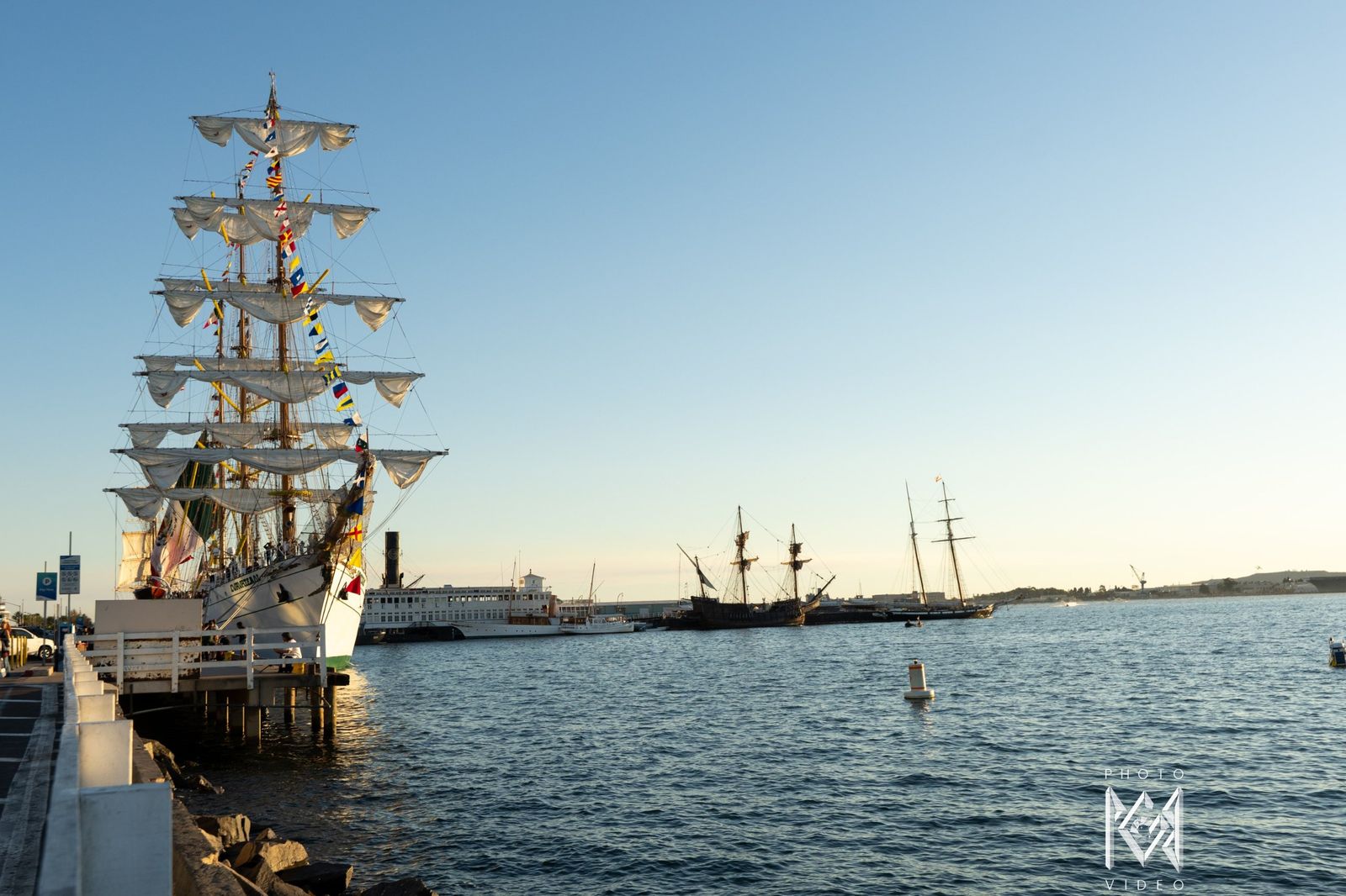 The ship moored at the pier, with a historic sailing ship across the bay