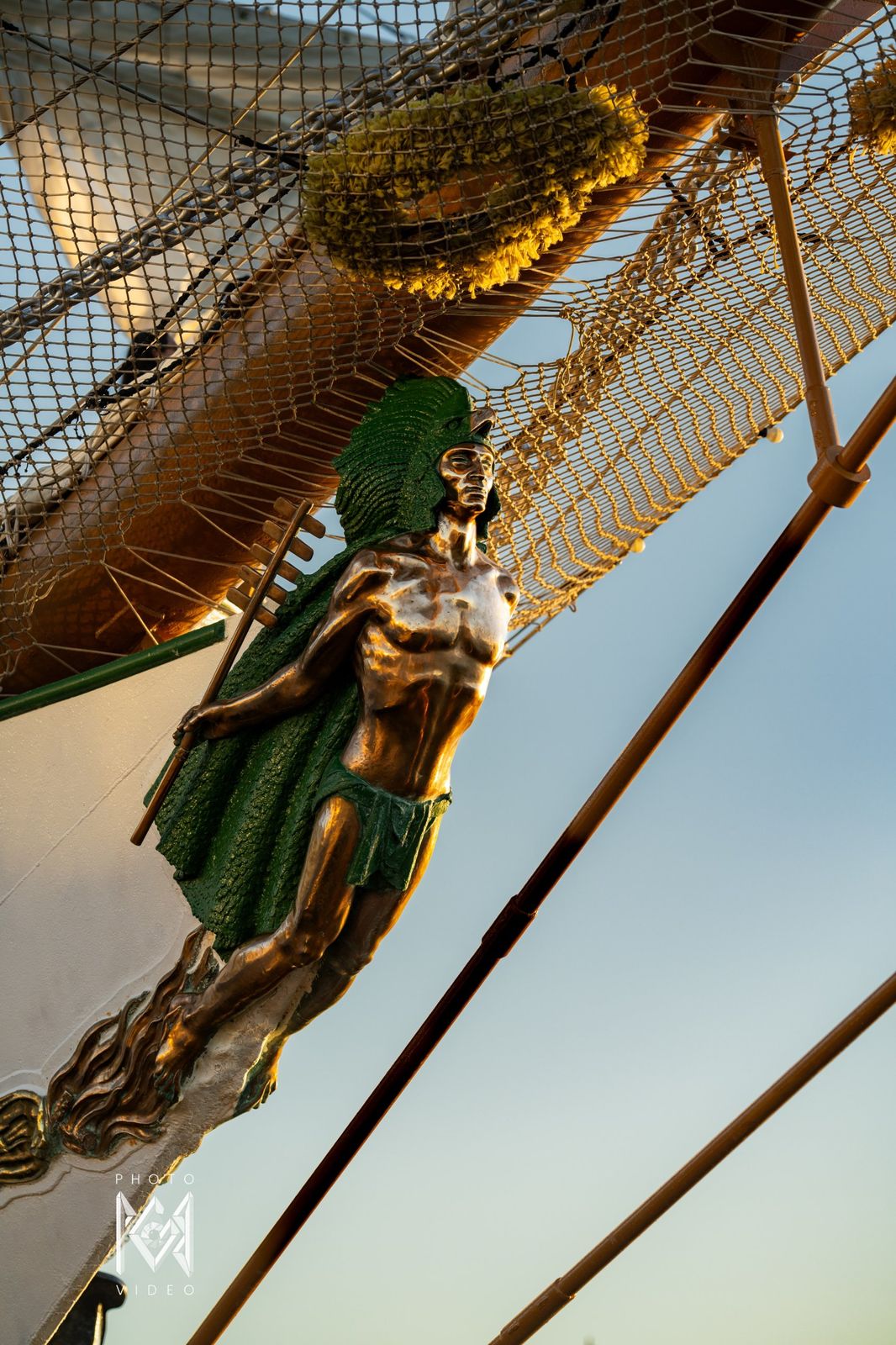 The bronze and green figurehead at the ship's bow, lit by evening sun