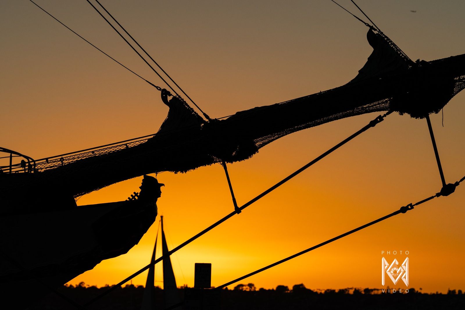 The bowsprit and rigging in silhouette against an orange sky