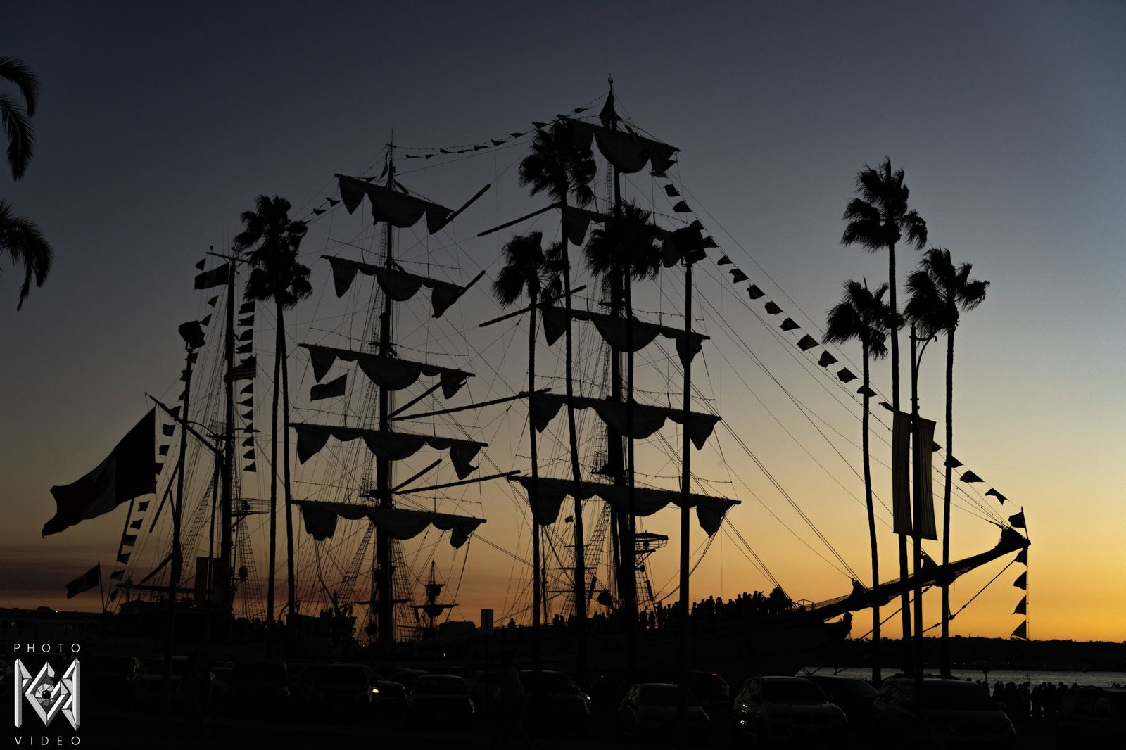The ship's masts, flags and palm trees in silhouette against the sunset