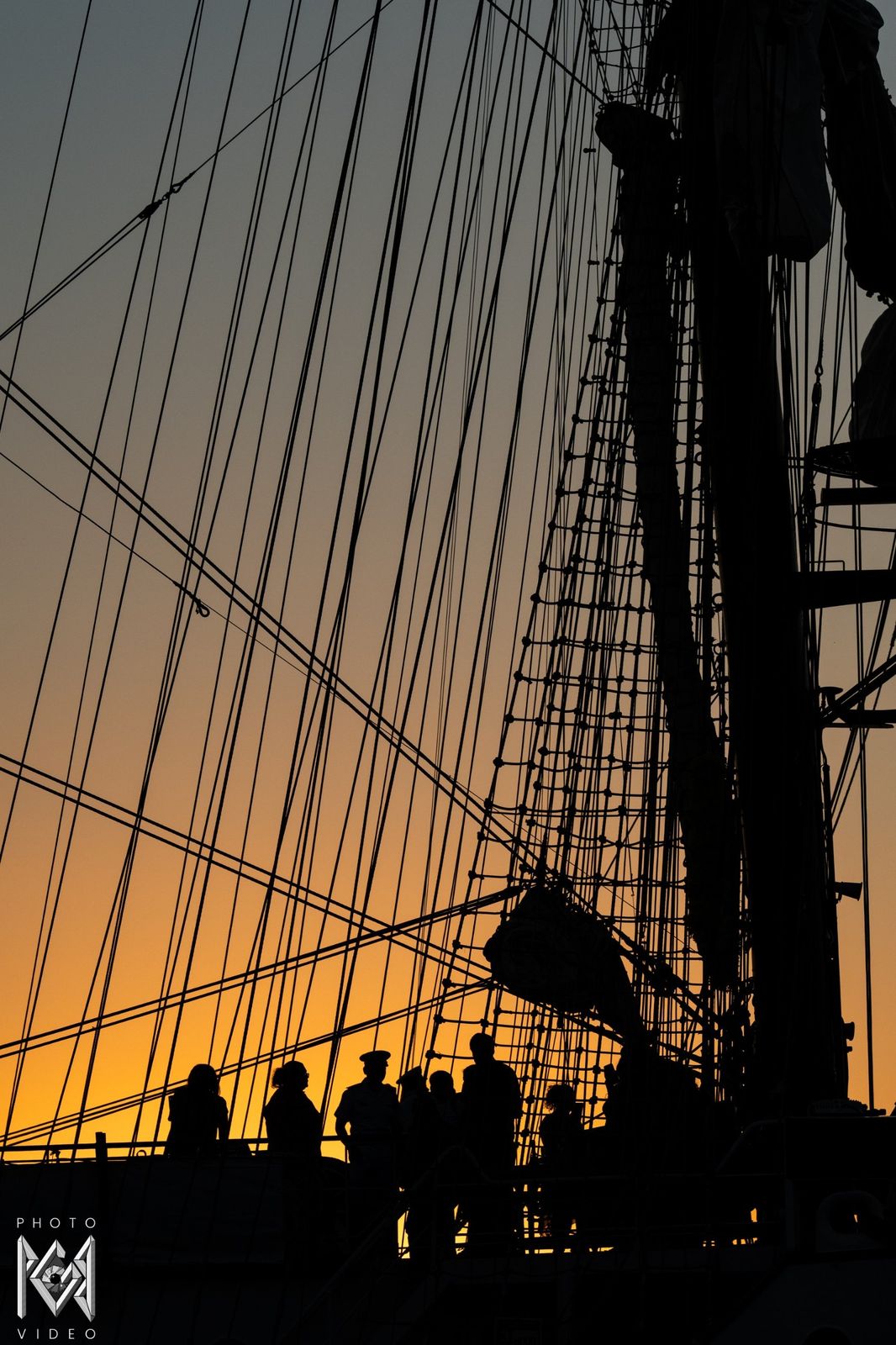 Rigging and masts in silhouette, with figures on deck below