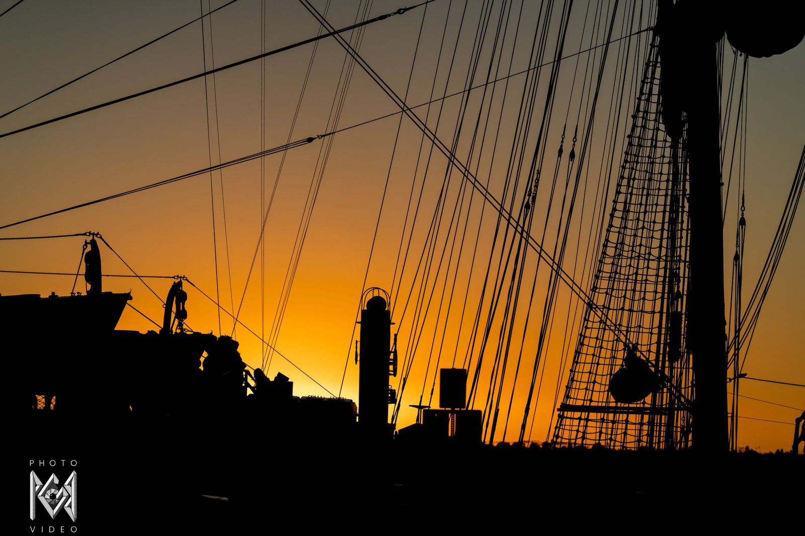 Rigging in silhouette against an orange sky, people on deck below
