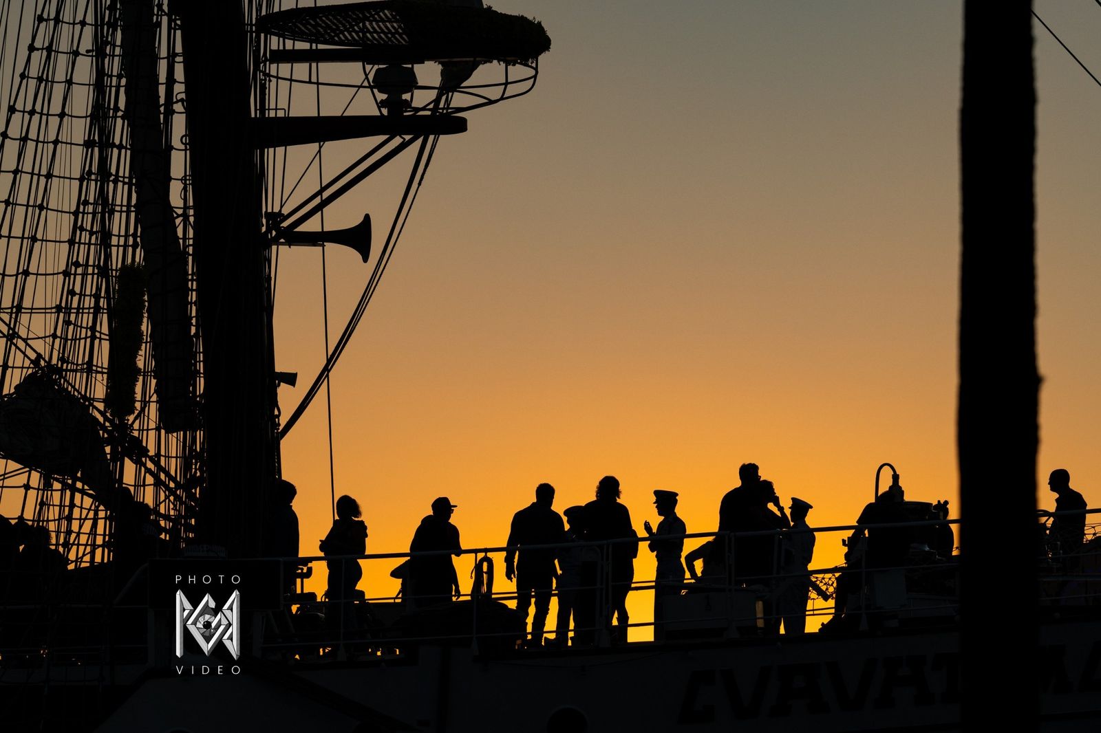 Visitors on the ship's deck in silhouette at sunset, her name lettering below