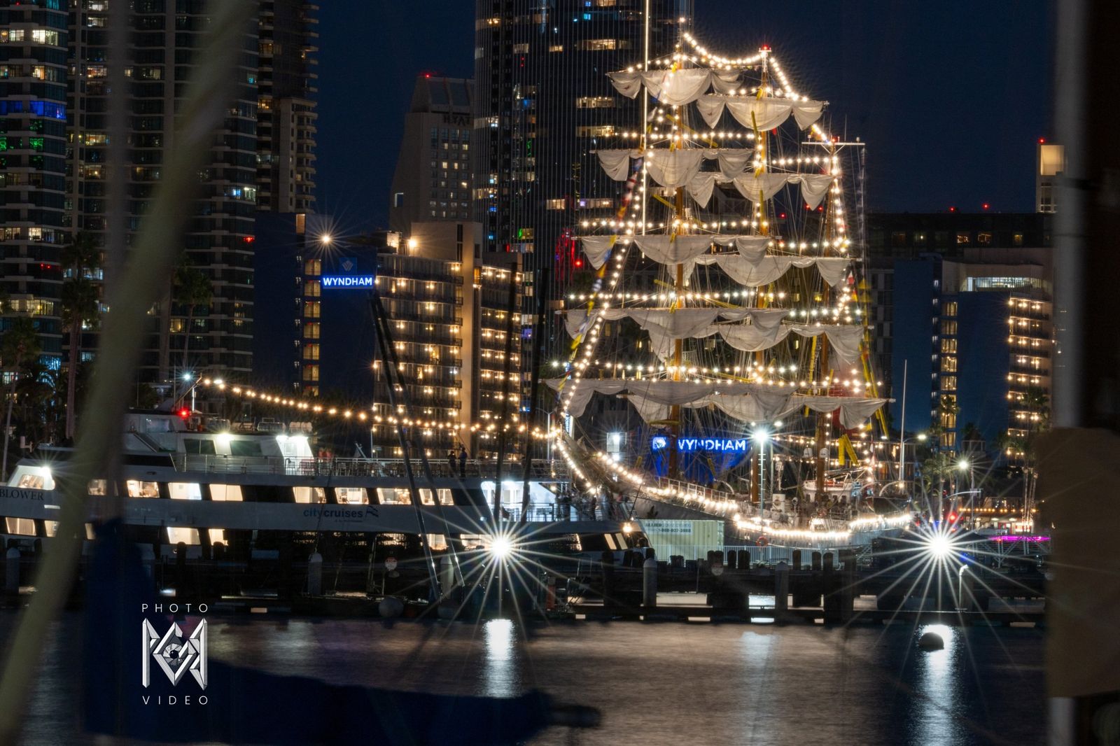 The ship outlined in lights between tall buildings, a boat in the foreground at night