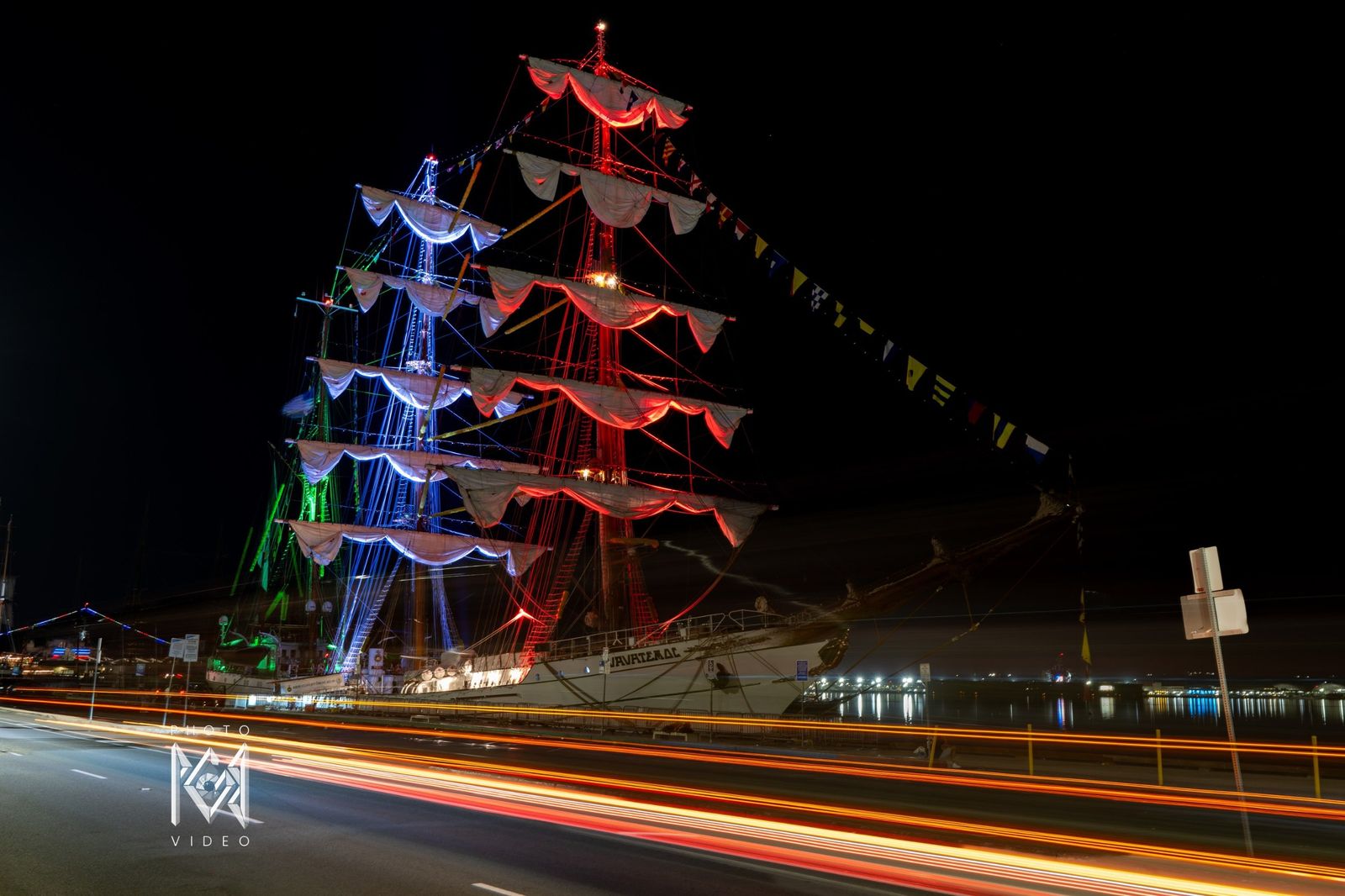 The ship's masts lit in red, white and blue above long light trails on a road