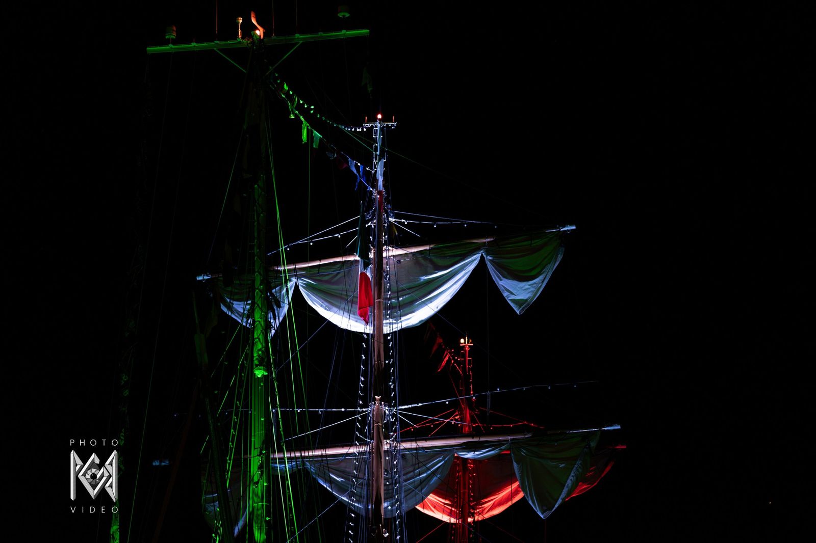 The ship's masts and sails lit in green and red in the dark