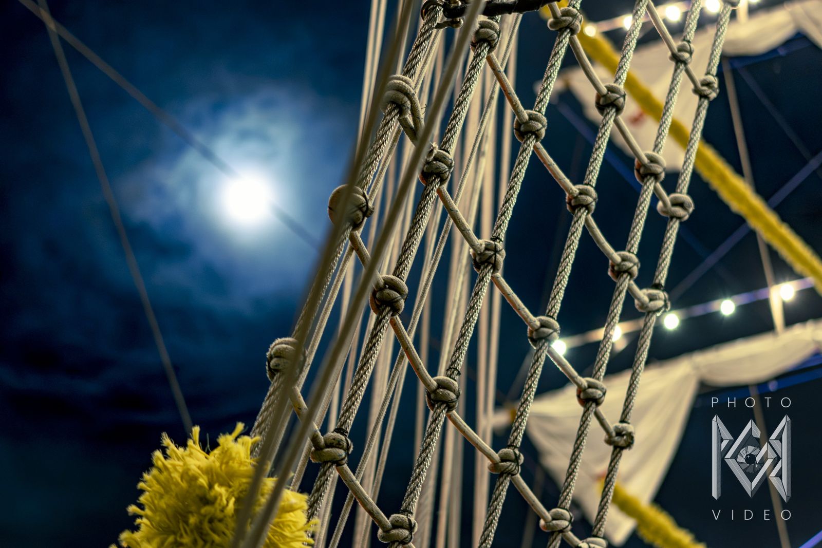 The full moon over the netting and rigging, with a yellow flower garland at the bottom