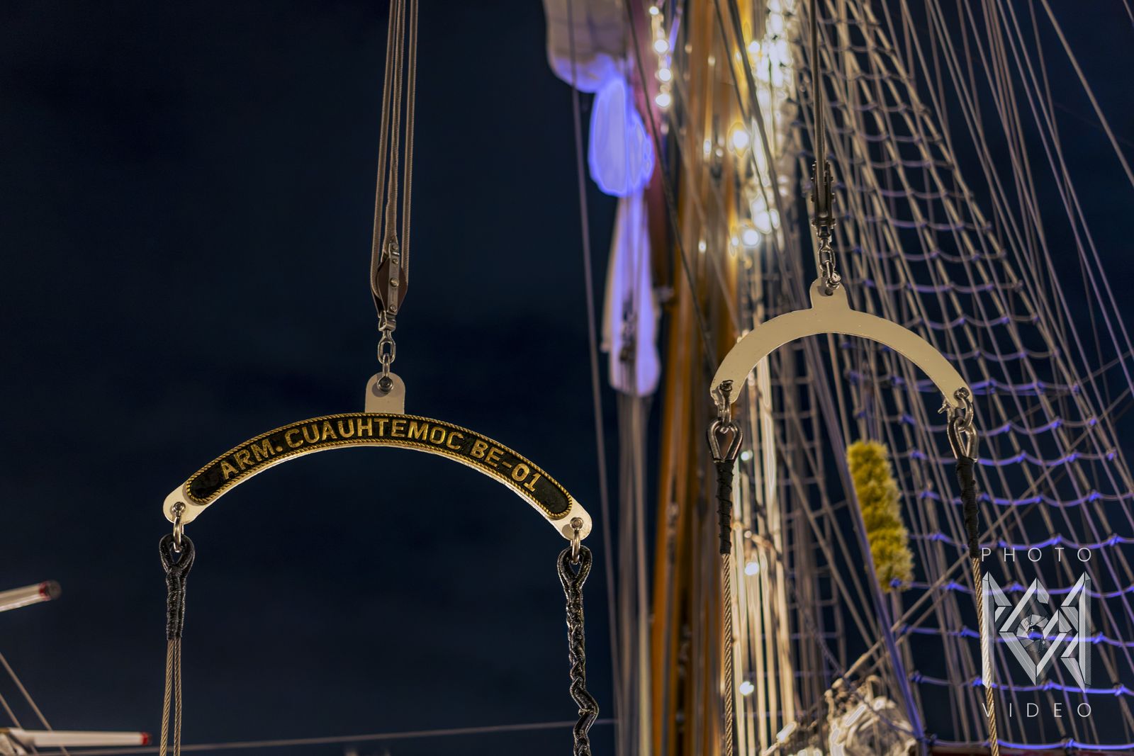 The brass nameplate hanging beside its empty frame, rigging and lit sails behind
