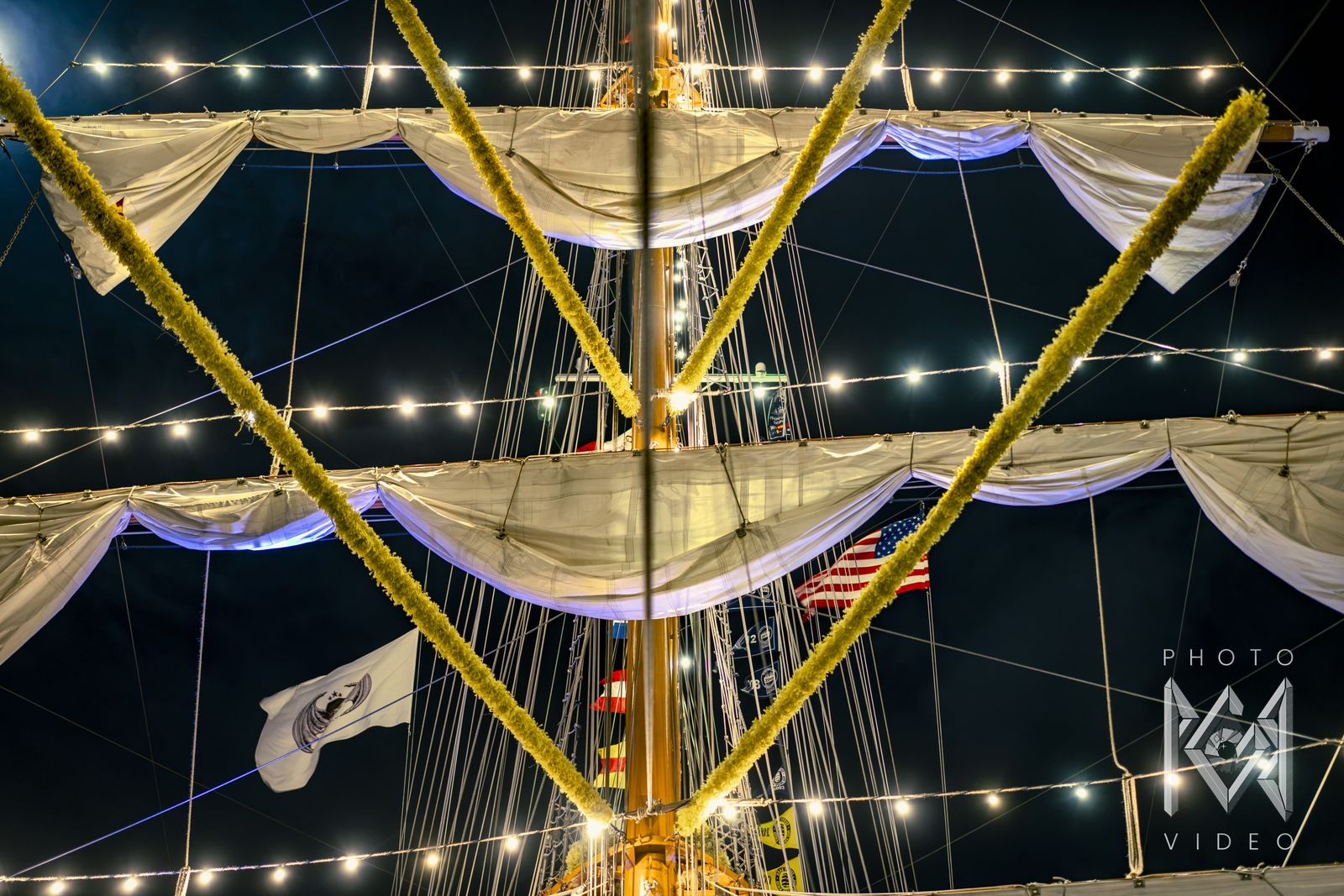 Yellow flower garlands and string lights crossing the ship's yards, flags below