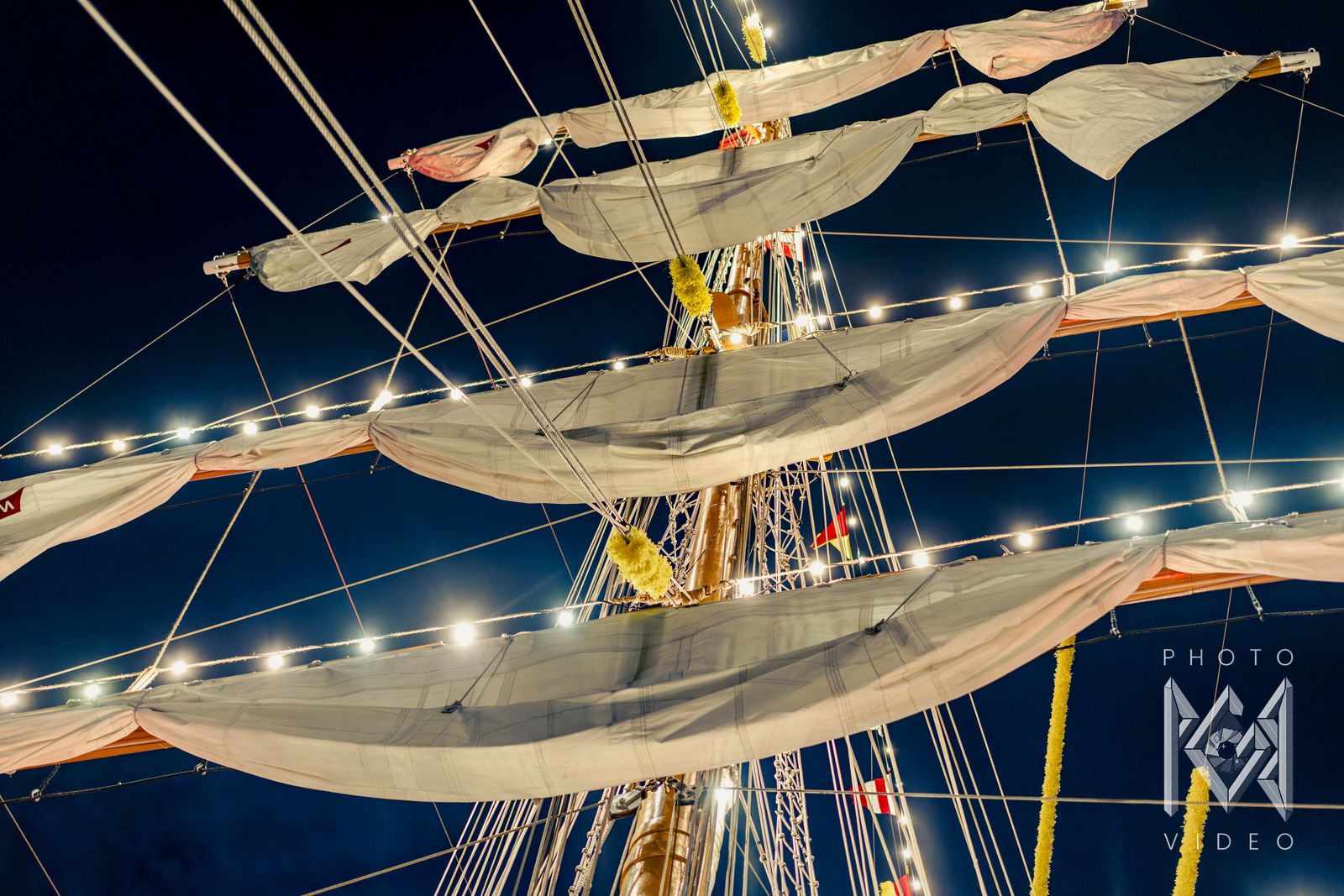 Furled sails and string lights on the yards at night