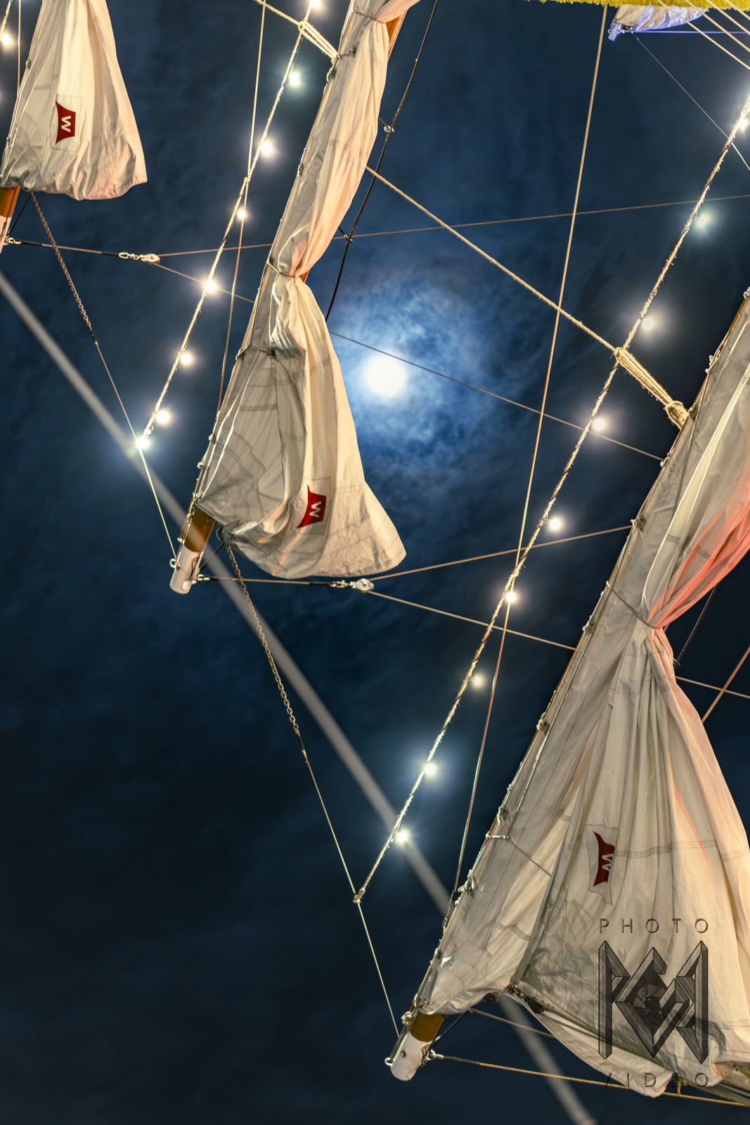 The full moon between furled sails and strings of lights