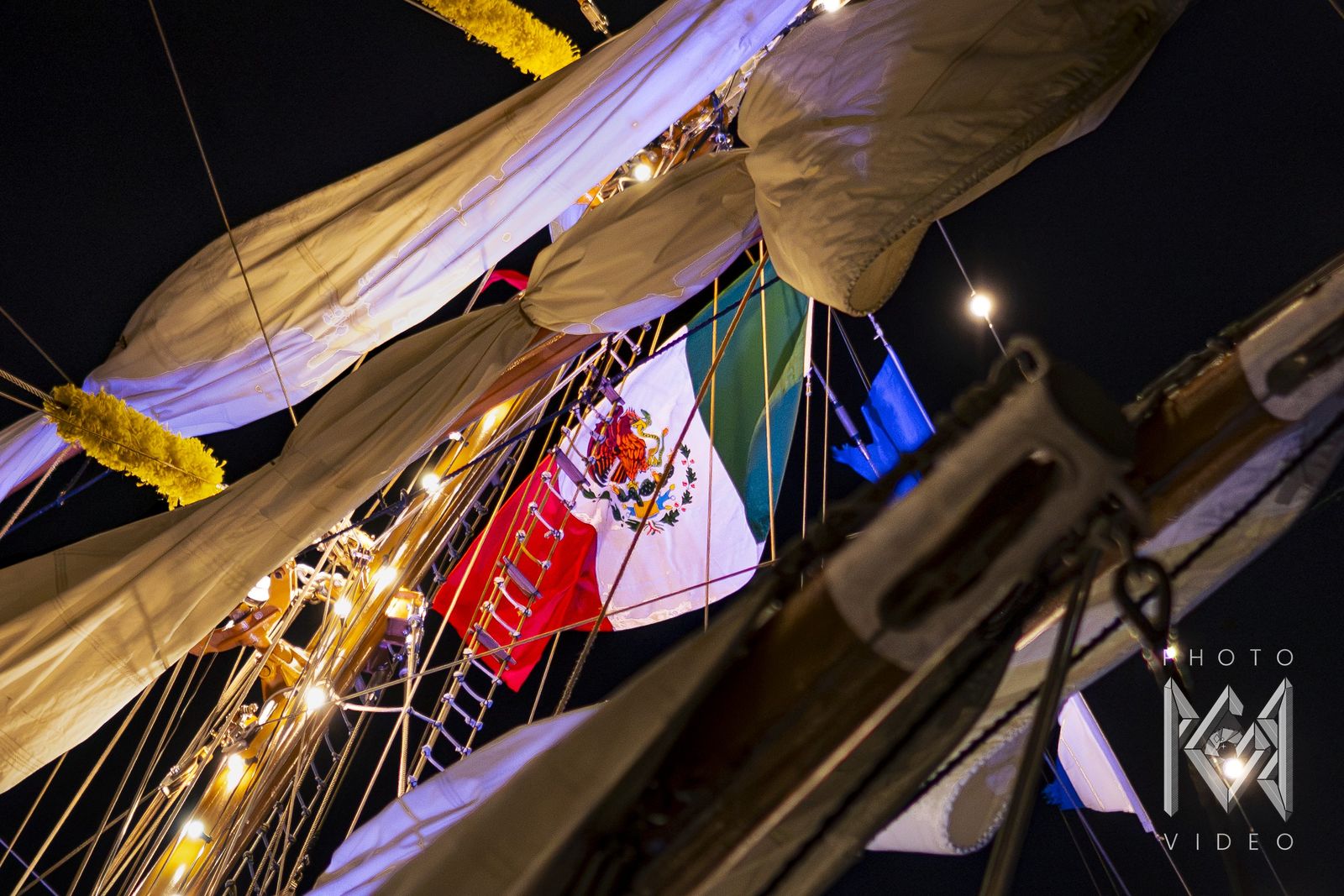 The ship's furled sails and the Mexican flag, seen from below at night