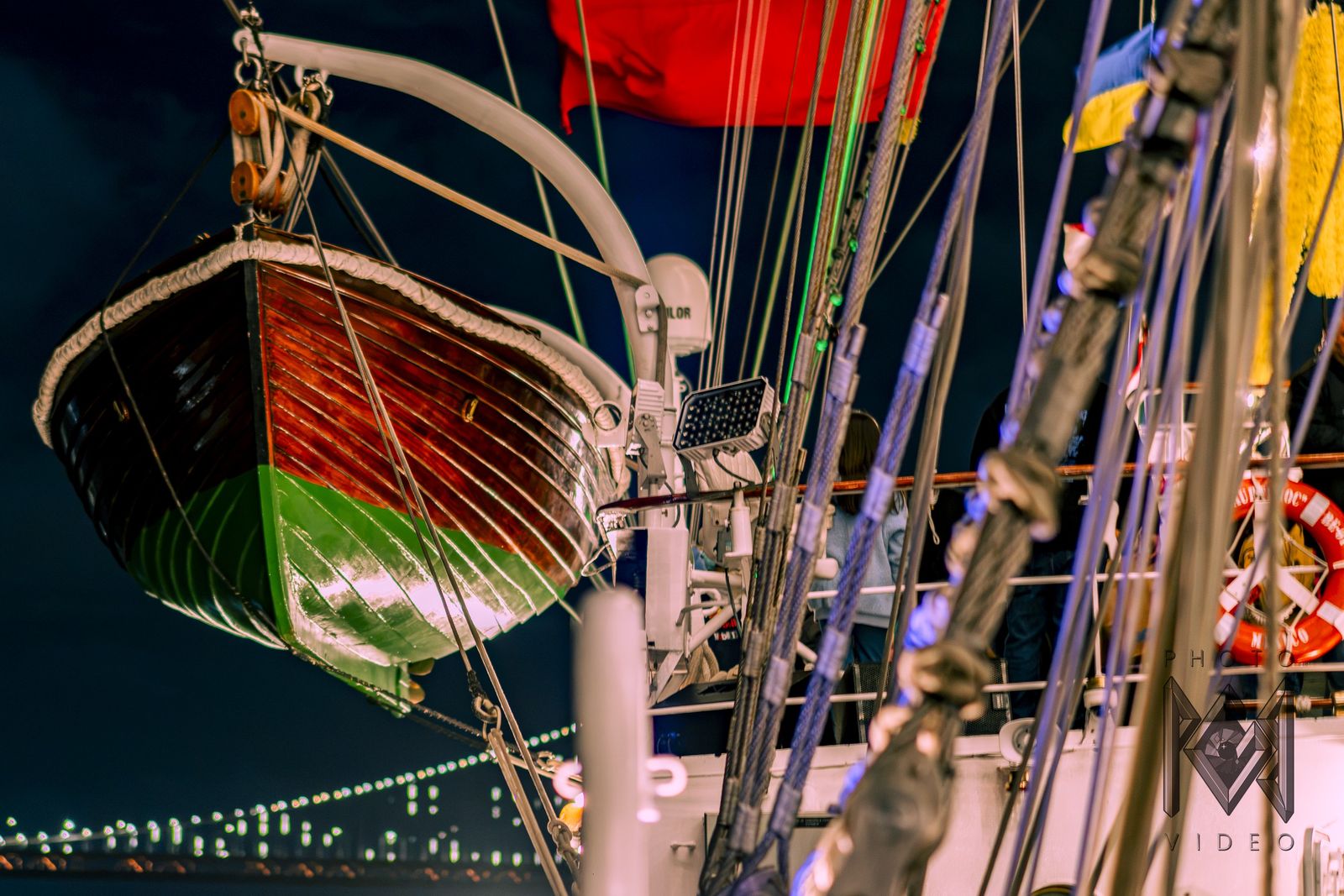 The ship's lifeboat hanging on its davit at night, the bridge's lights beyond