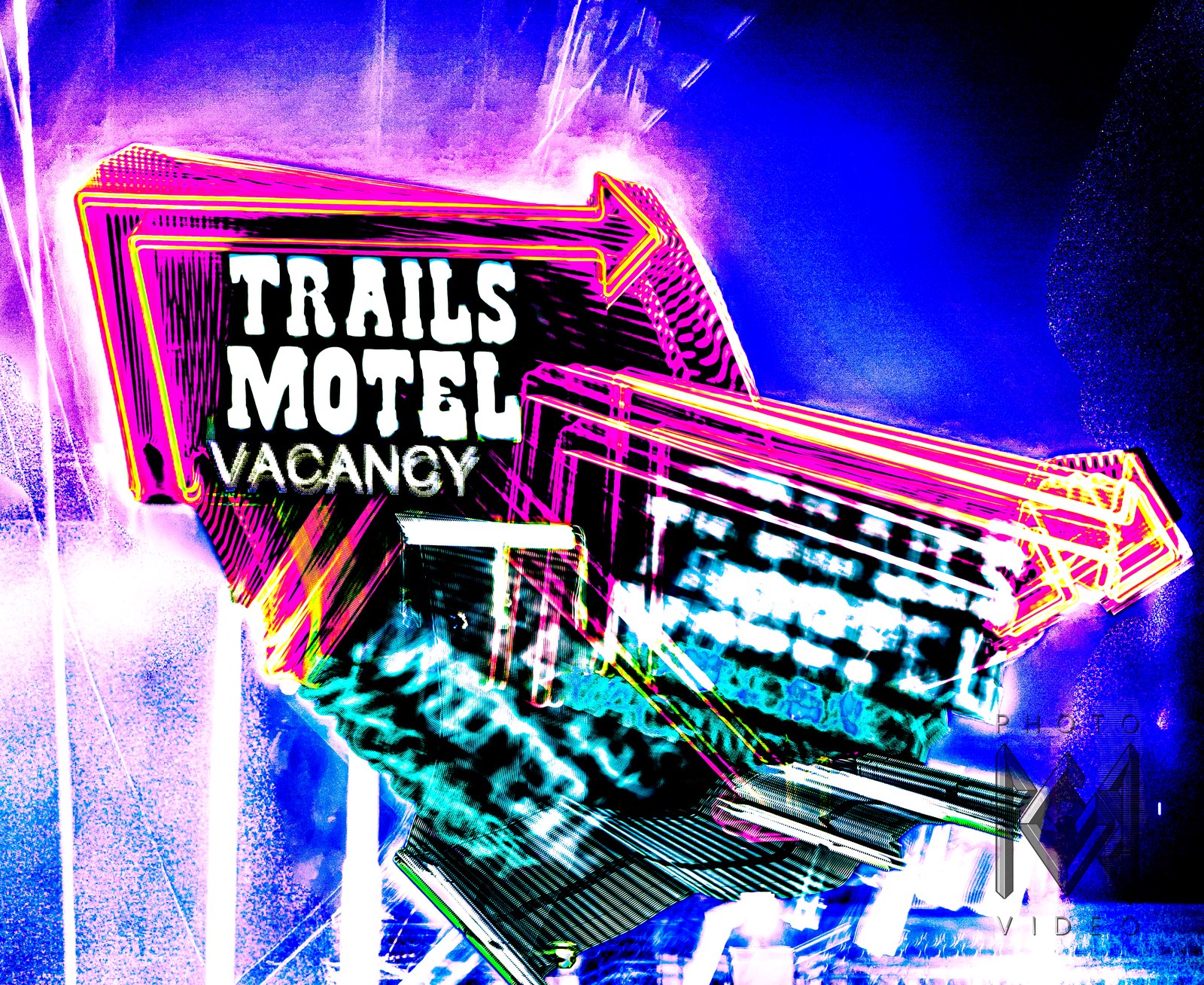 A neon Trails Motel Vacancy sign, an arrow in pink, red and yellow, glowing against a blue-violet night sky