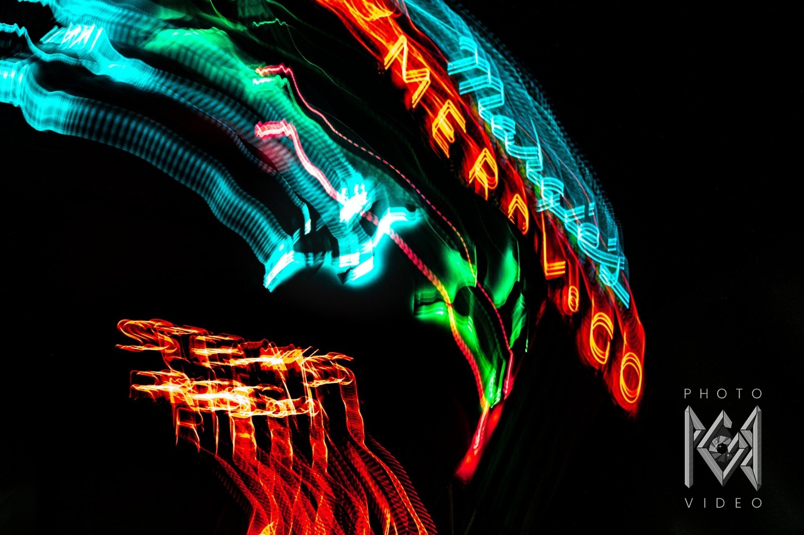 A curving sweep of cyan, green and red neon, with MERRY-GO lettering rising along the arc and a red STEAKS RIBS sign blurred below
