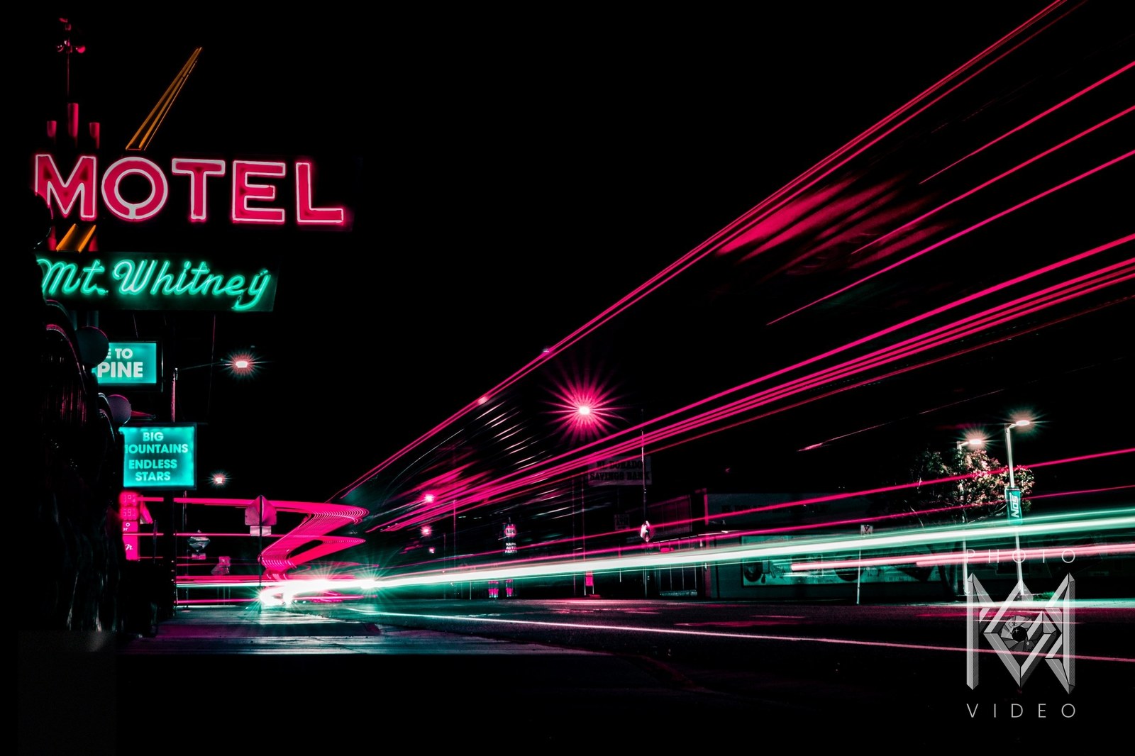 Lone Pine motel neon, MOTEL and Mt. Whitney signs glowing at left, with pink and teal light trails streaking down the street at night