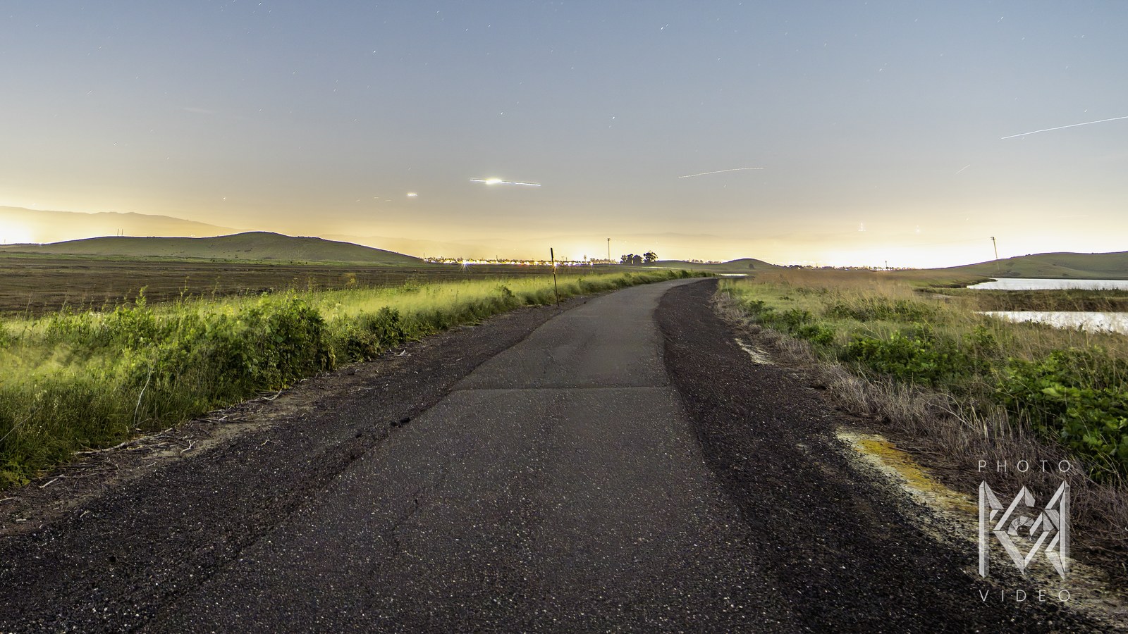 A paved levee path curving past marsh and grass under a clear blue dusk sky, city glow on the horizon