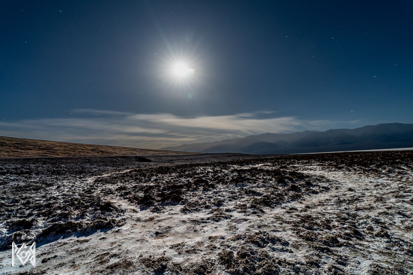 A hazy moon low over the salt flats, white crust running toward a distant ridge
