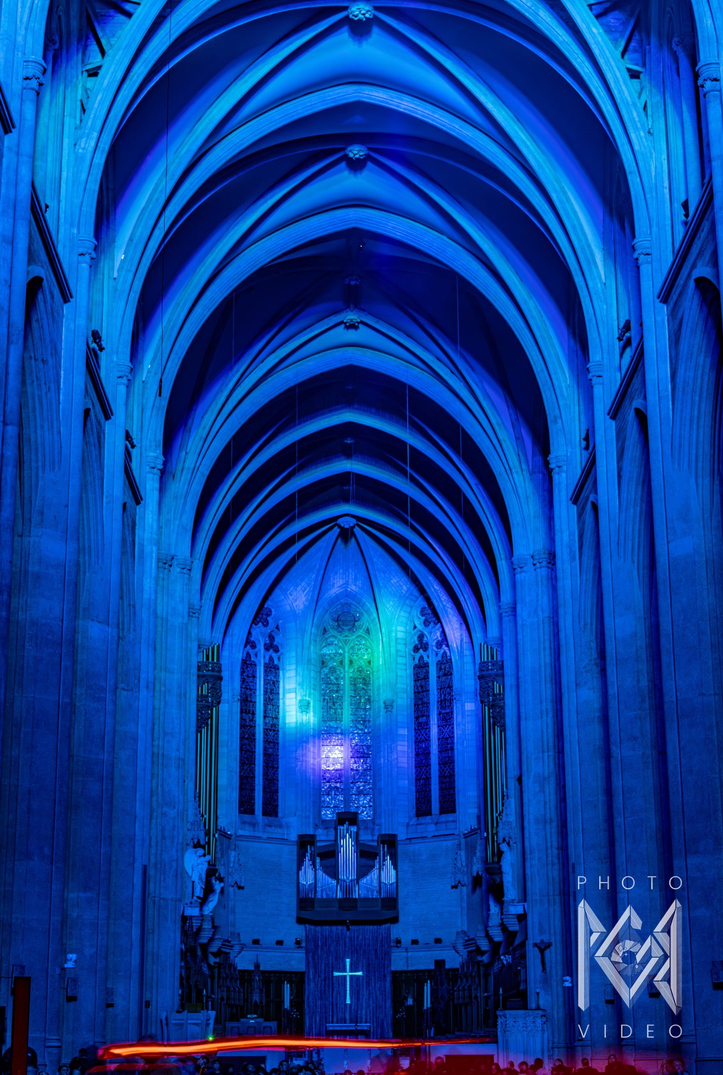 A cathedral nave bathed in blue light, ribbed vaults receding toward the organ and stained glass, with a streak of red light below