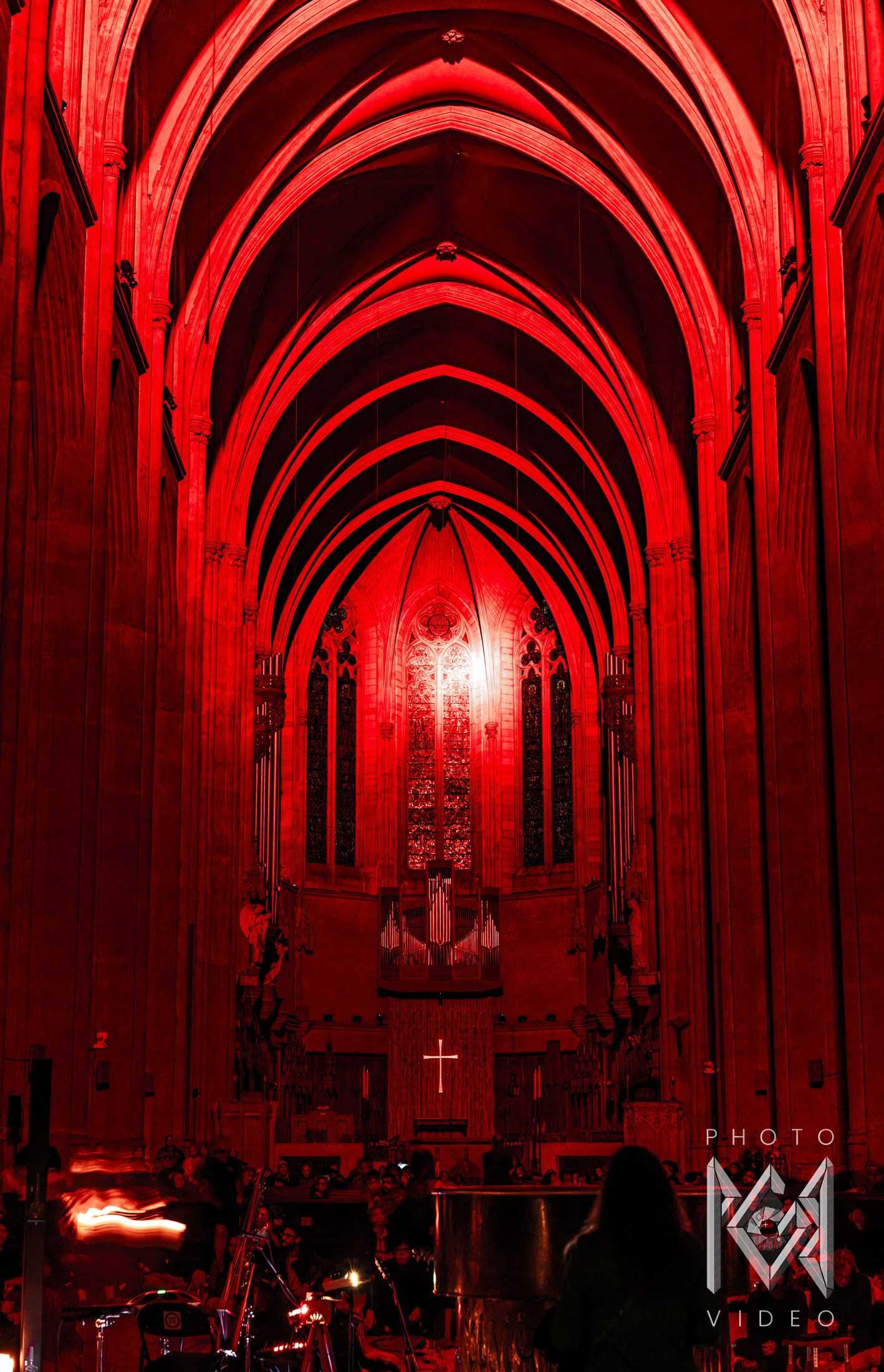 A cathedral nave lit deep red during a concert, its vaults glowing above the organ, altar and seated audience